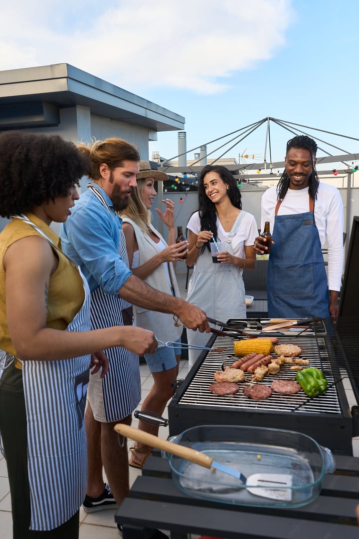Cheerful friends enjoying a barbecue party on a rooftop, grilling food and having drinks together