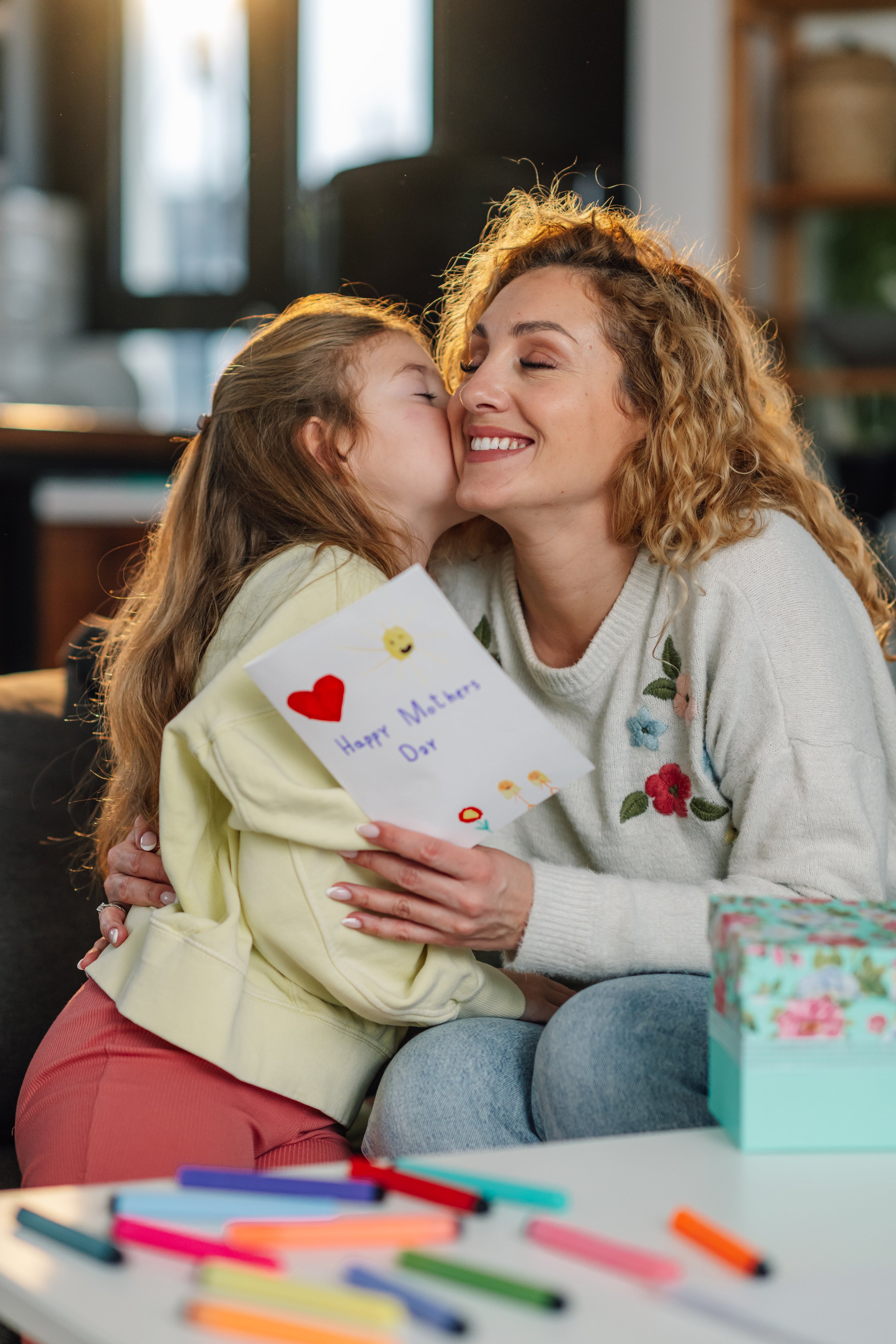 Daughter kissing her mother on the cheek and giving her a handmade greeting card for mother's day
