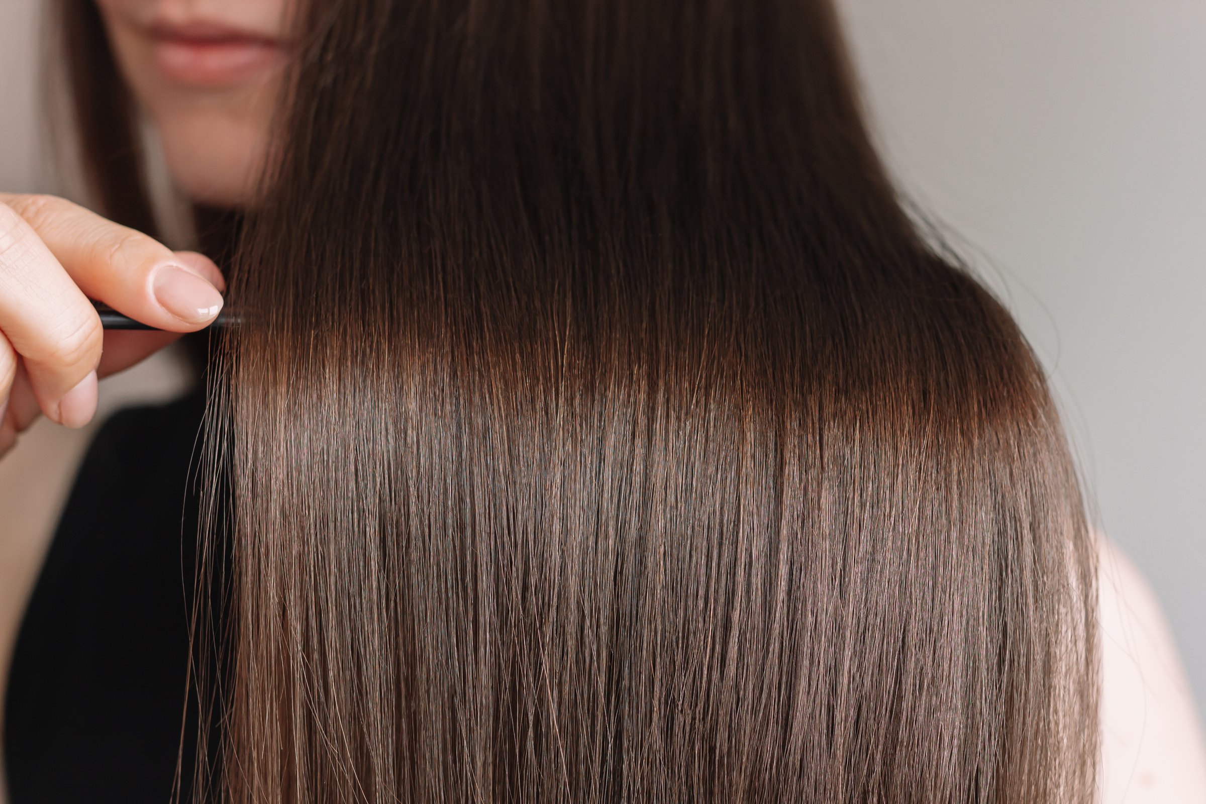 Young Caucasian brunette woman demonstrating her beautiful long shiny smooth healthy hair close-up