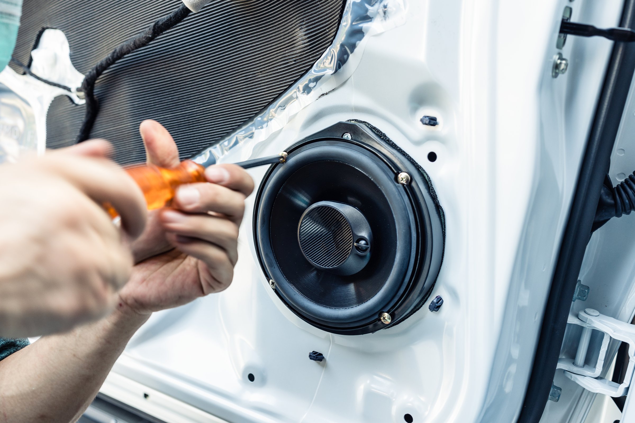 Mechanic using screwdriver screwing drywall screw with car speaker on vehicle door panel in garage
