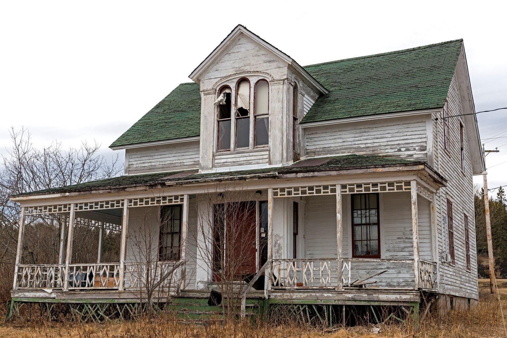 An old, abandoned house. Windows at the top are broken, the paint is peeling, and the front porch os falling down. Overcast sky.