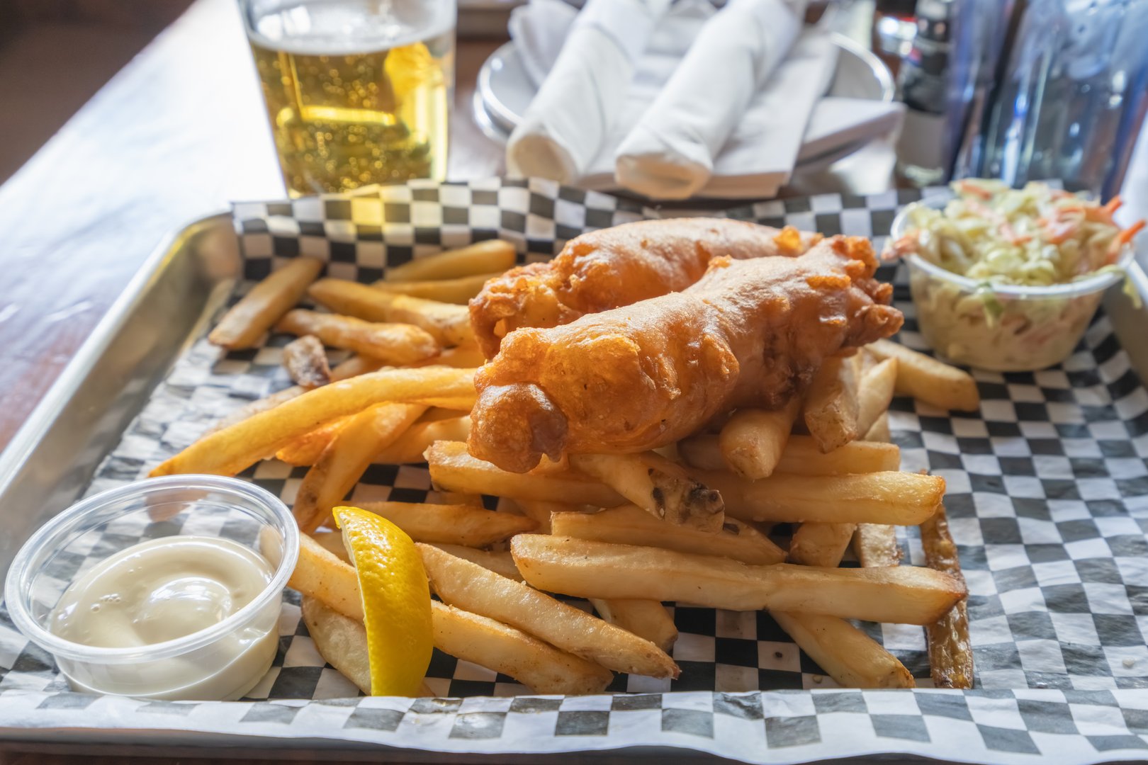 Freshly fried fish and chips with a side of creamy coleslaw and beer on a rustic wooden table.
