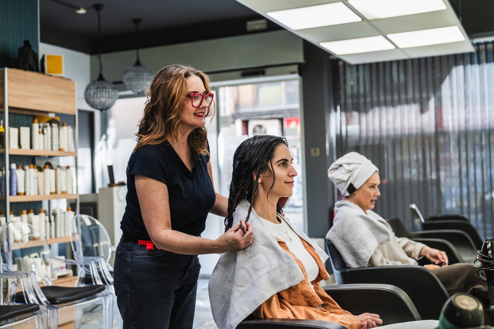 Hairdresser preparing a young woman's hair for a beauty treatment in a modern salon, with other clients waiting