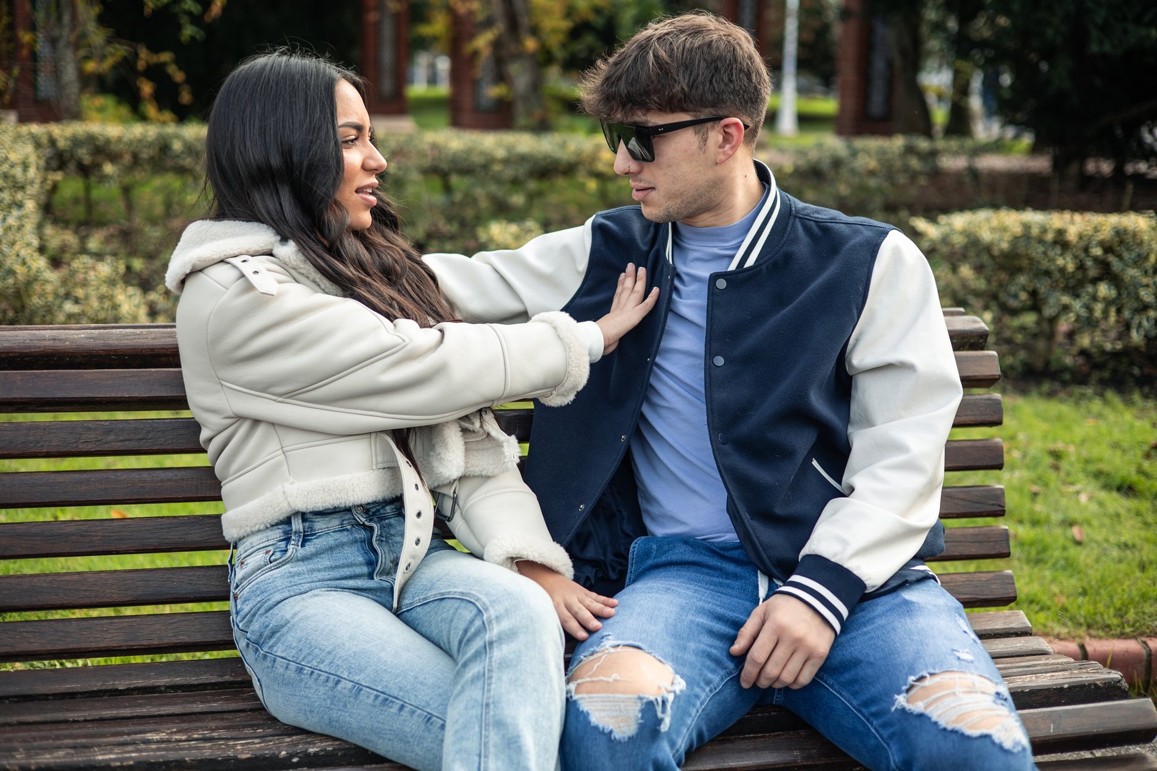 Angry latin student girl rejecting her caucasian boyfriend sitting on a bench outdoors