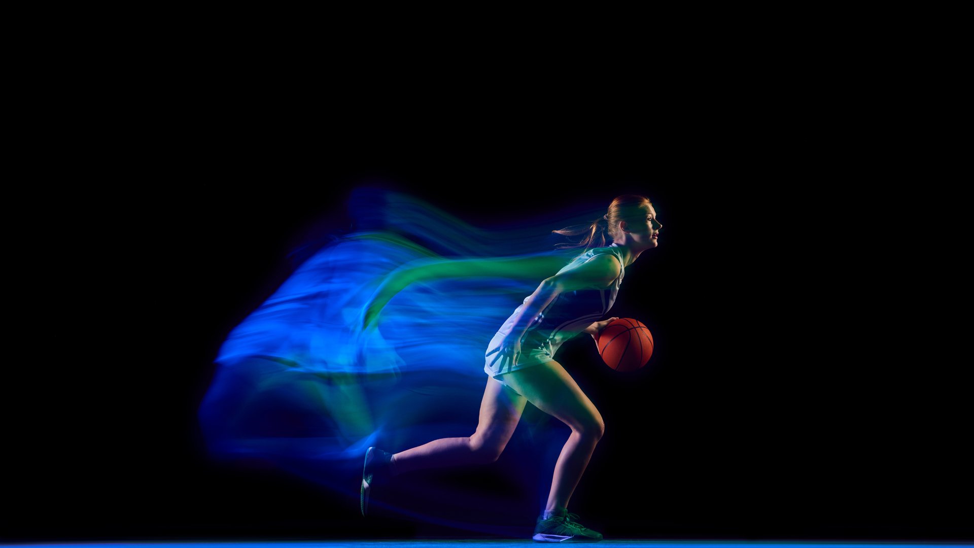 Female athlete sprinting with basketball through blue motion trail. Concept of speed performance, fitness campaign visuals, and creative content for sports brands.
