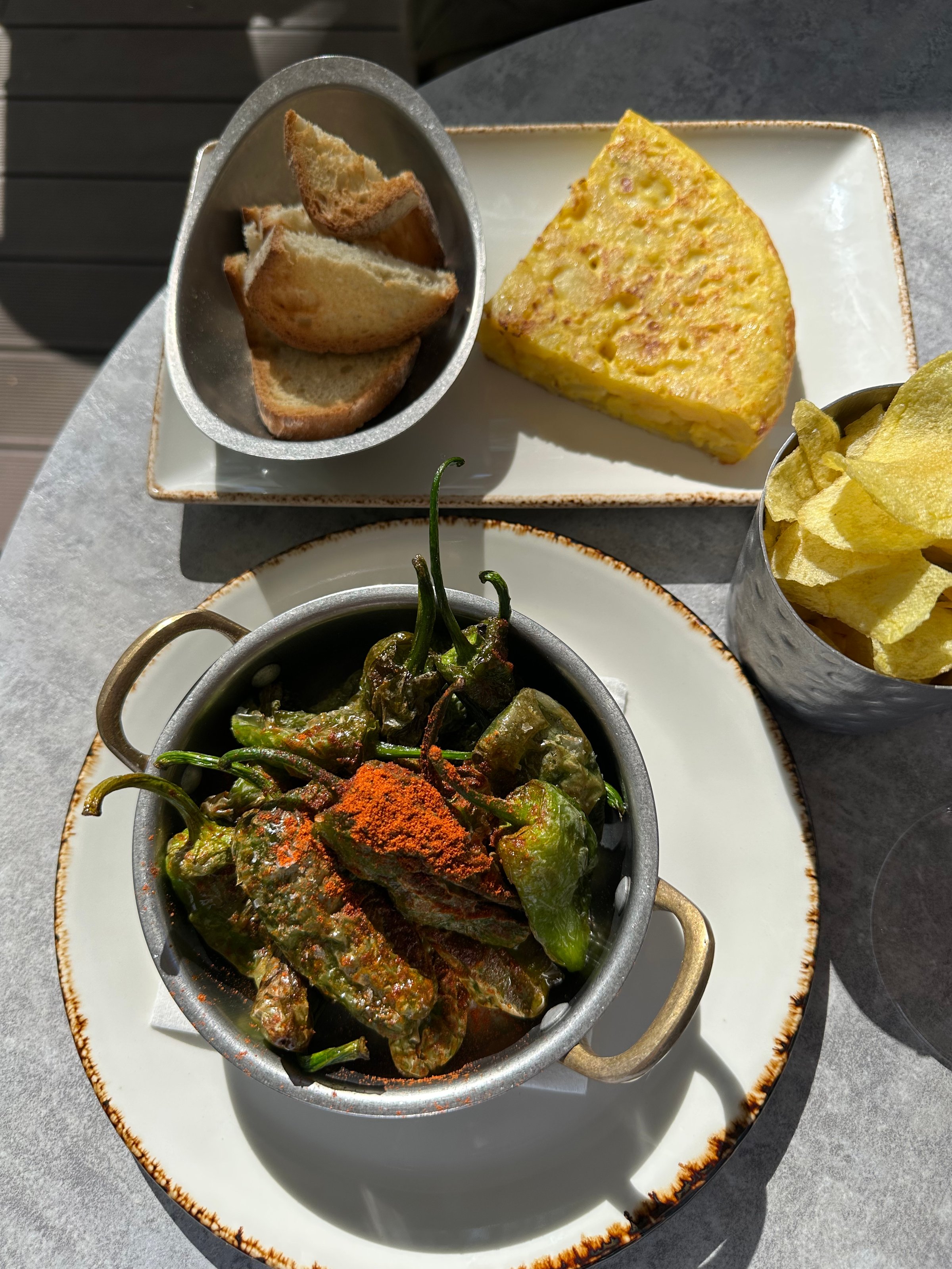 Delicious tapas and cocktails enjoyed under the sun — a cozy Mediterranean moment with padrón peppers, Spanish tortilla, fresh bread, and crispy chips, perfect for relaxing and connecting