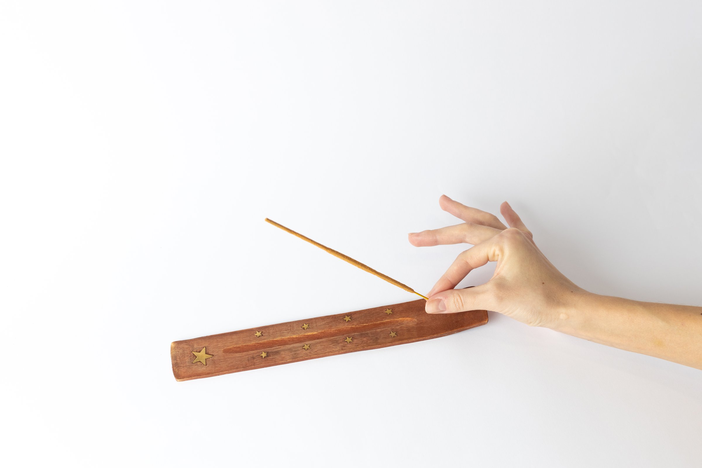 close-up on a white background on a long brown stand with stars for incense sticks, a woman's hand puts a new beige meditation stick on a traditional set