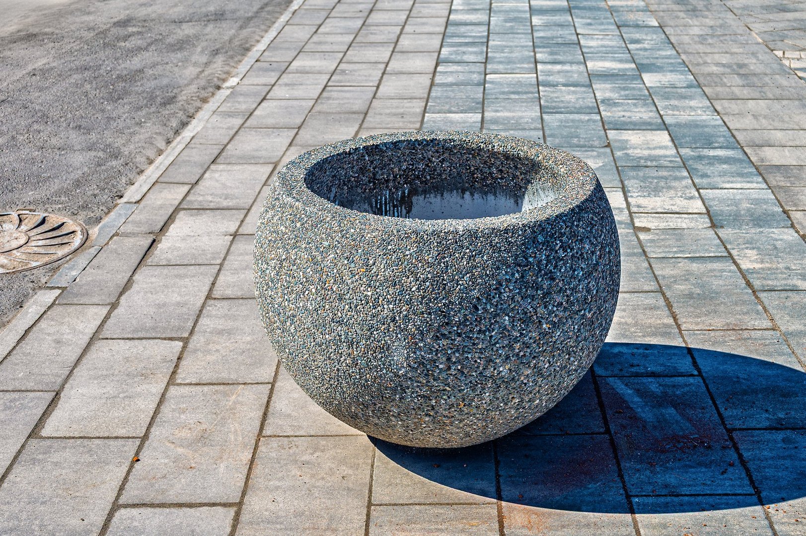 A stone flower pot on the paving stones of a city pedestrian side walk.