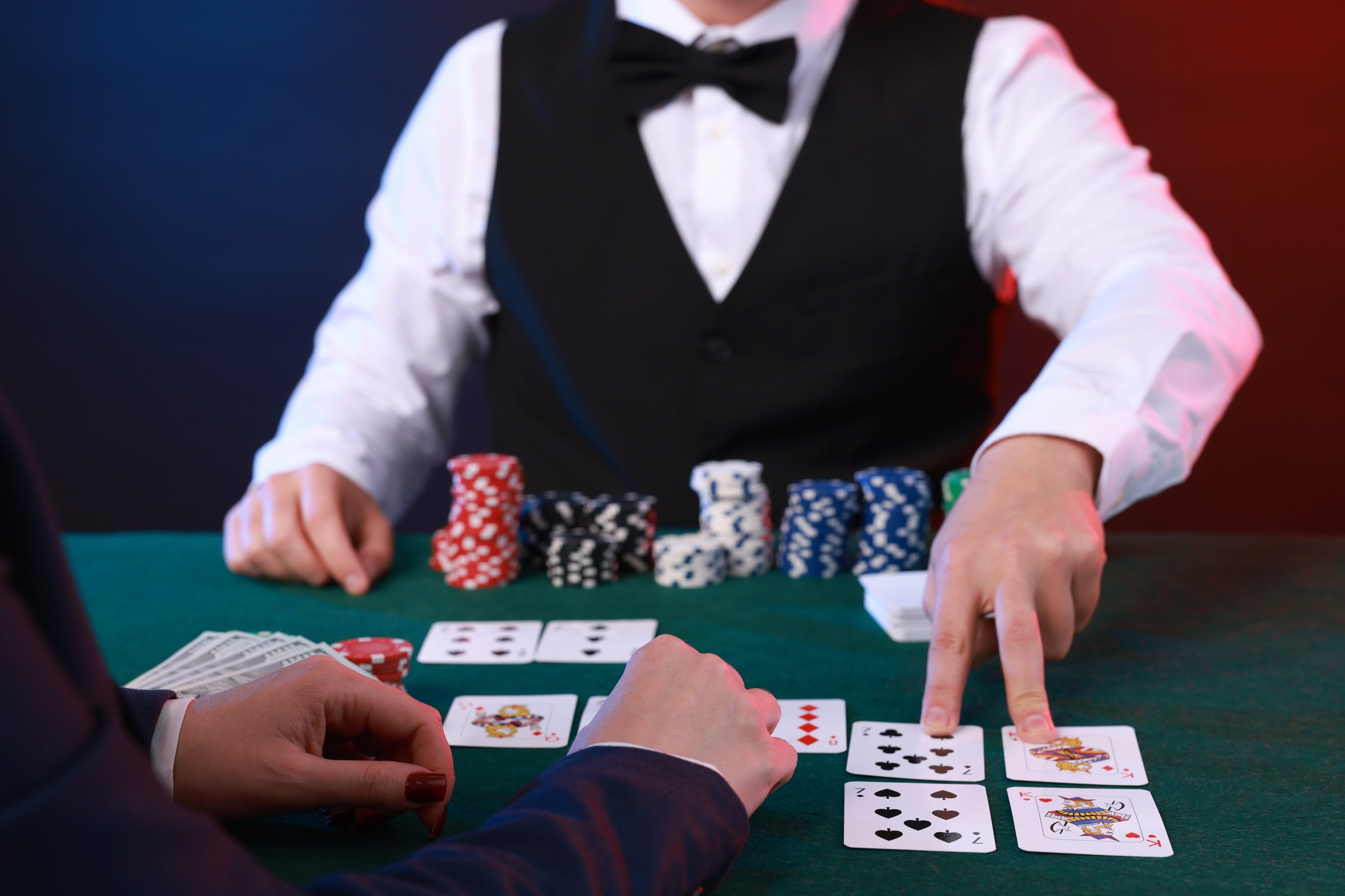 Professional croupier and gambler at table with playing cards and casino chips, closeup