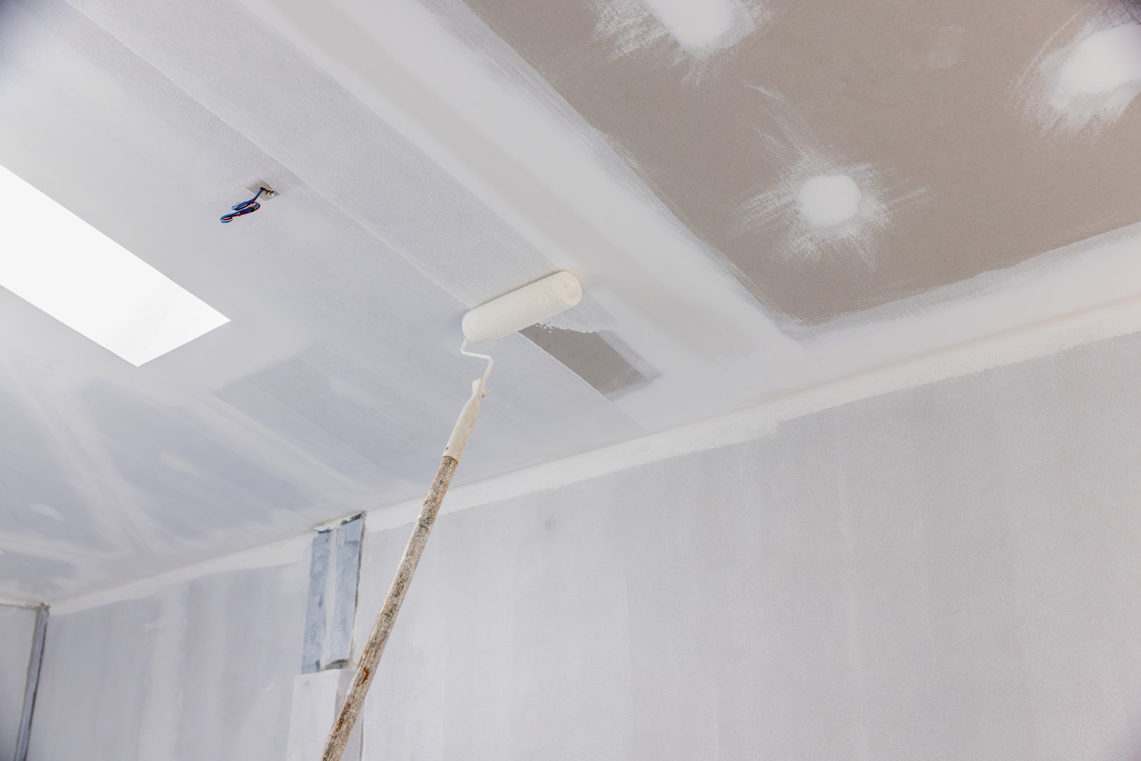 Handyman painting gypsum ceiling panel in kitchen