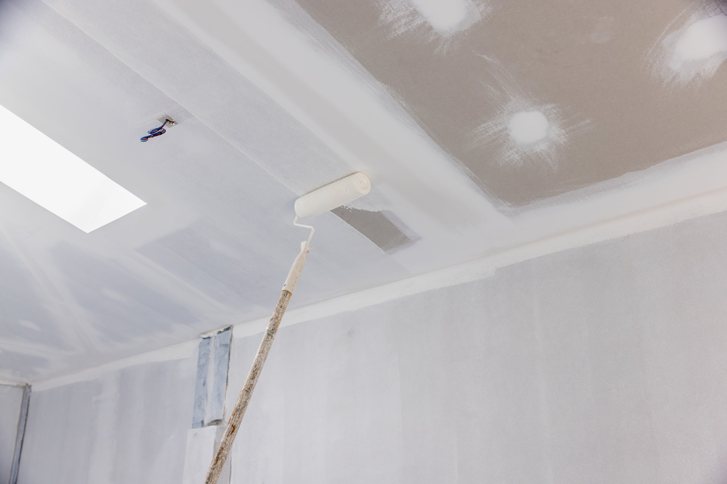 Handyman painting gypsum ceiling panel in kitchen.