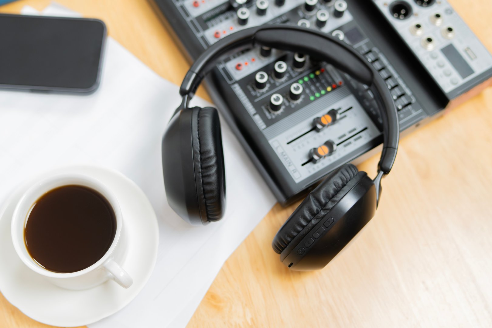 Headphones on a sound mixer with cup of coffee on a wooden desk at home studio podcast. Top view, selective focus.
