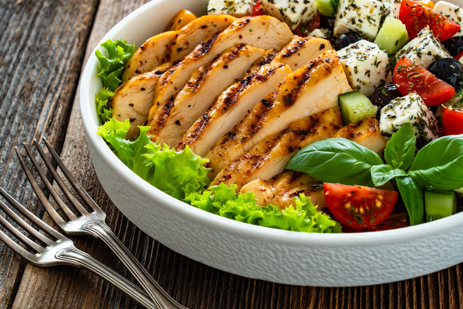 Grilled sliced chicken breast and Greek salad on wooden table