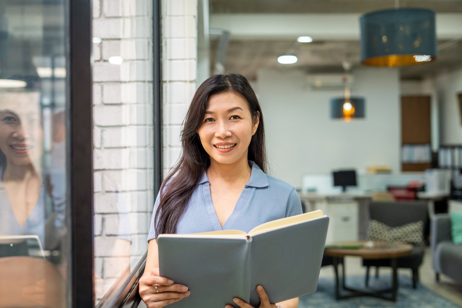 portrait of businesswoman in smart casual wear, standing in office with note book and looking into camera