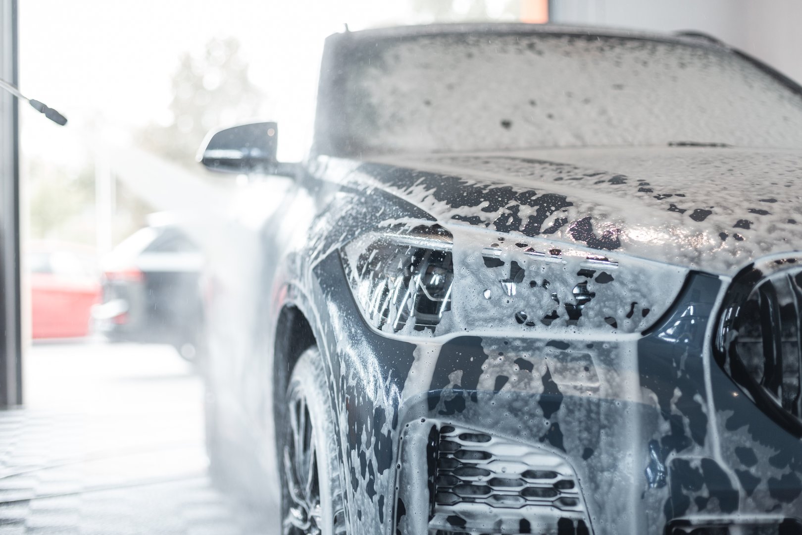 Modern SUV car in white foam is washed at car wash. Detailing center