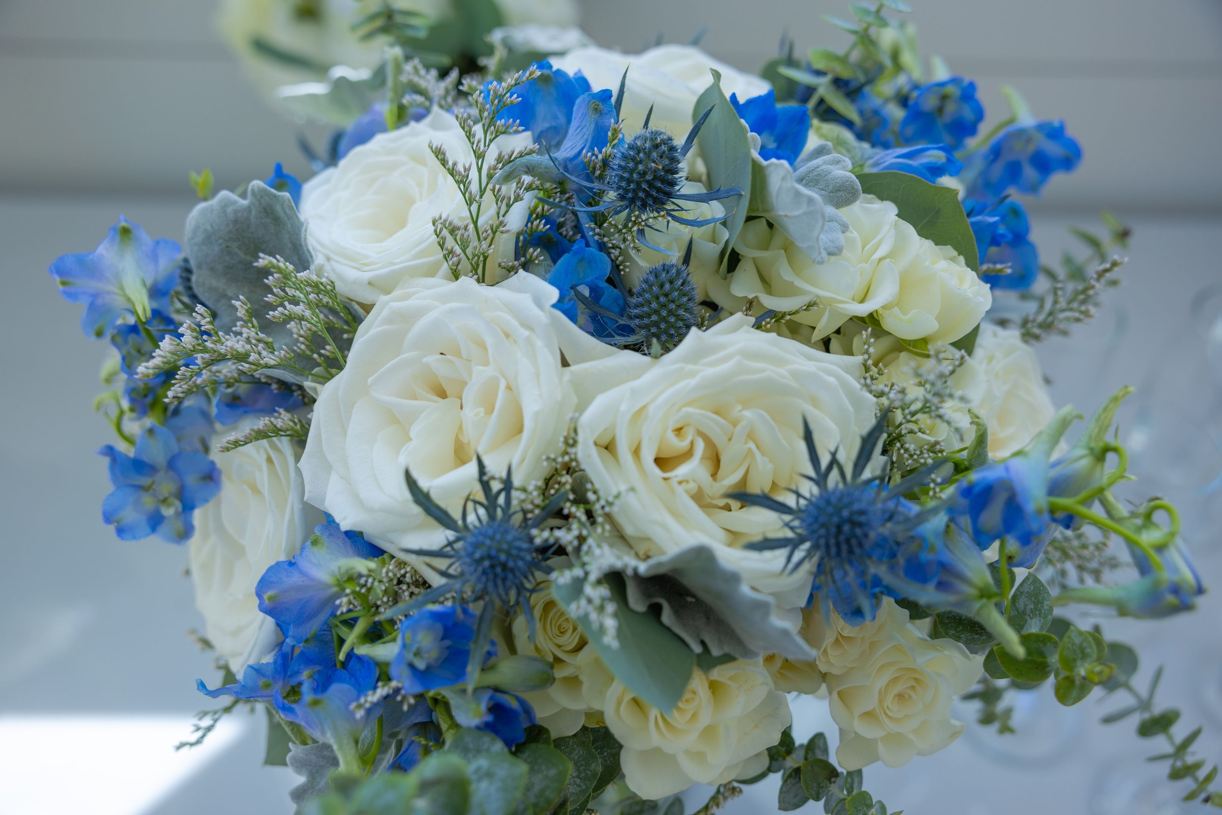 Elegant bouquet of white roses and blue flowers with lush greenery, perfect for weddings or special occasions.