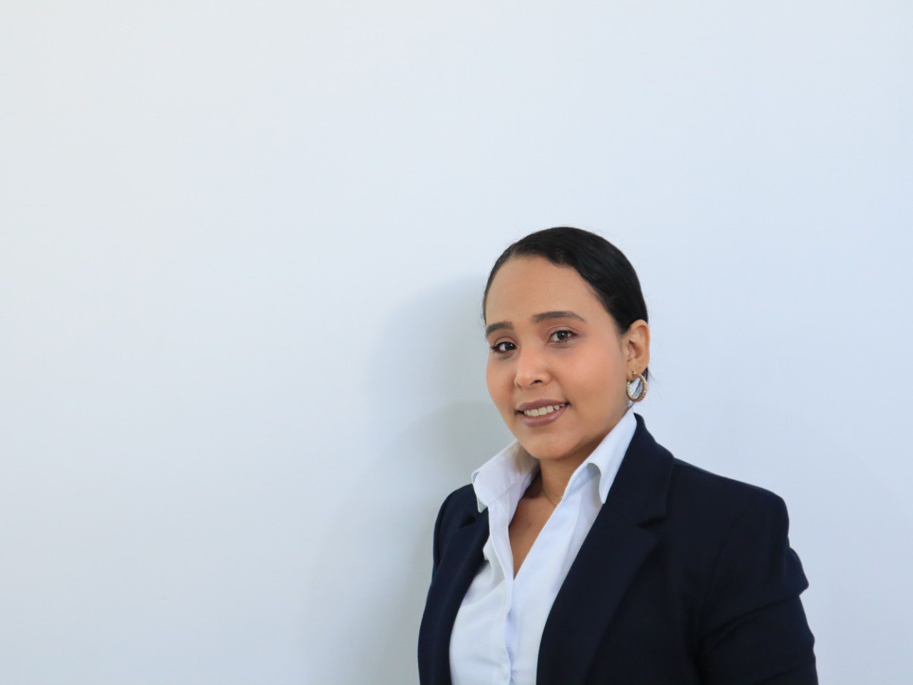 Woman in a dark blazer and white shirt, smiling against a plain white background.
