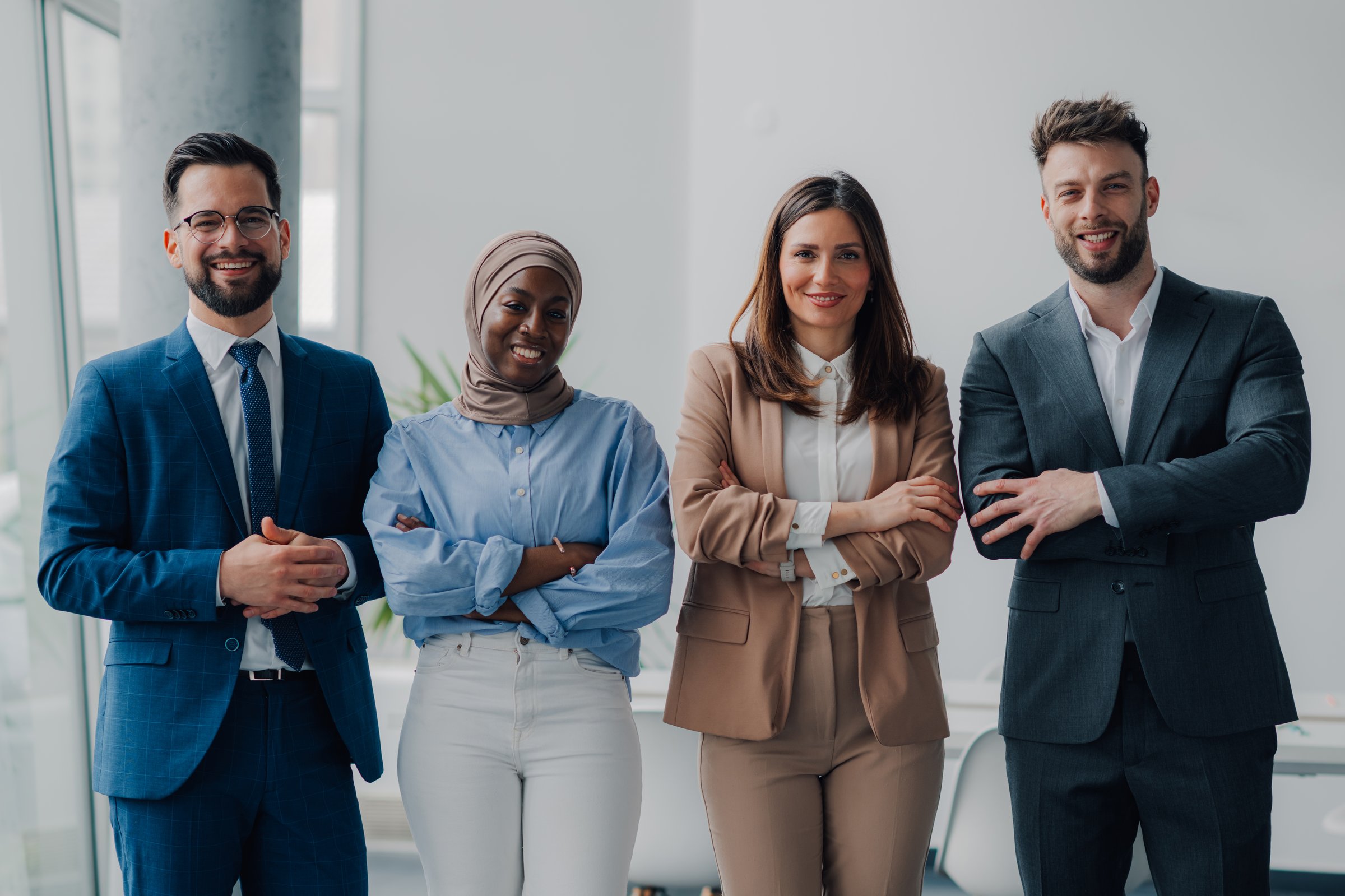 Four businesspeople smiling with arms crossed, showing teamwork and confidence in a modern office
