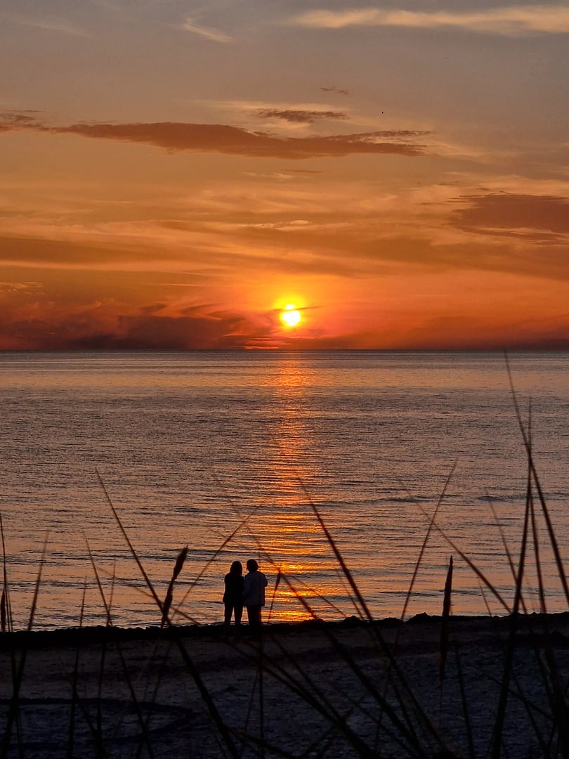 A stunning sunset over calm sea waters and two silhouttes of a couple enjoying the breathtaking view and calmness