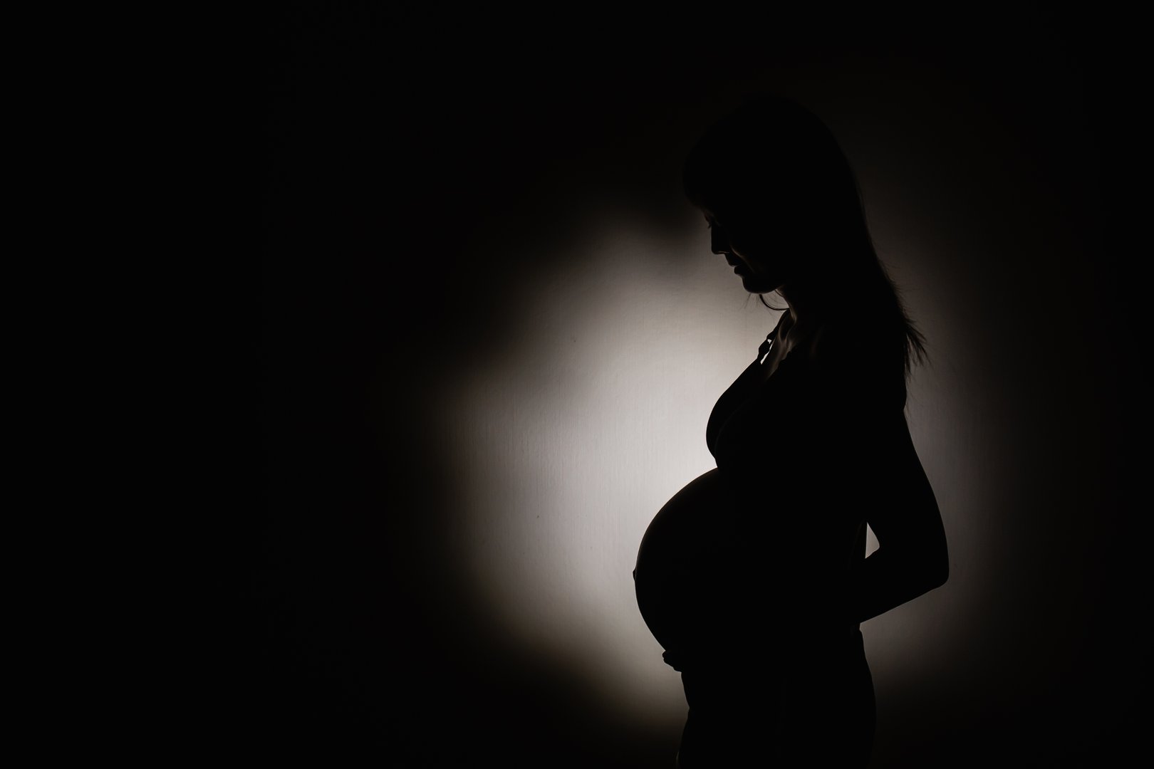 Pregnant woman's shadow with light in the center in room background. Concept photography copy space.