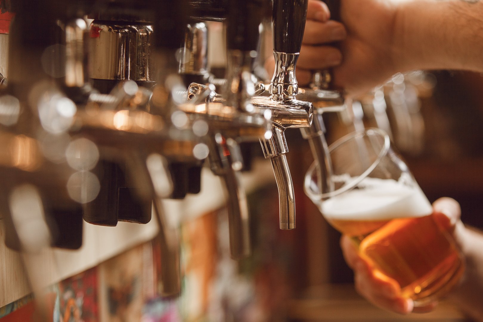 Skilled bartender skillfully fills glass with golden beer from tap in bustling bar during the evening.