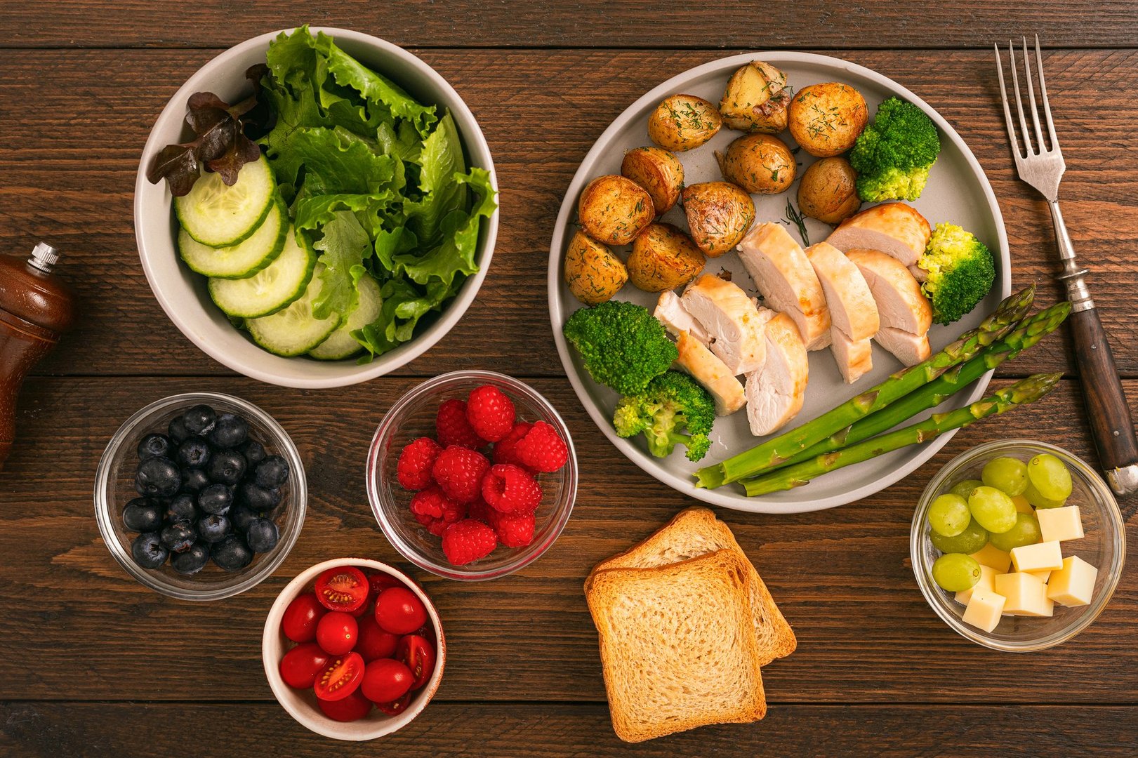 Top view of balanced clean healthy eating meal with grilled chicken roasted potatoes asparagus broccoli salad tomatoes berries and cheese on wooden background