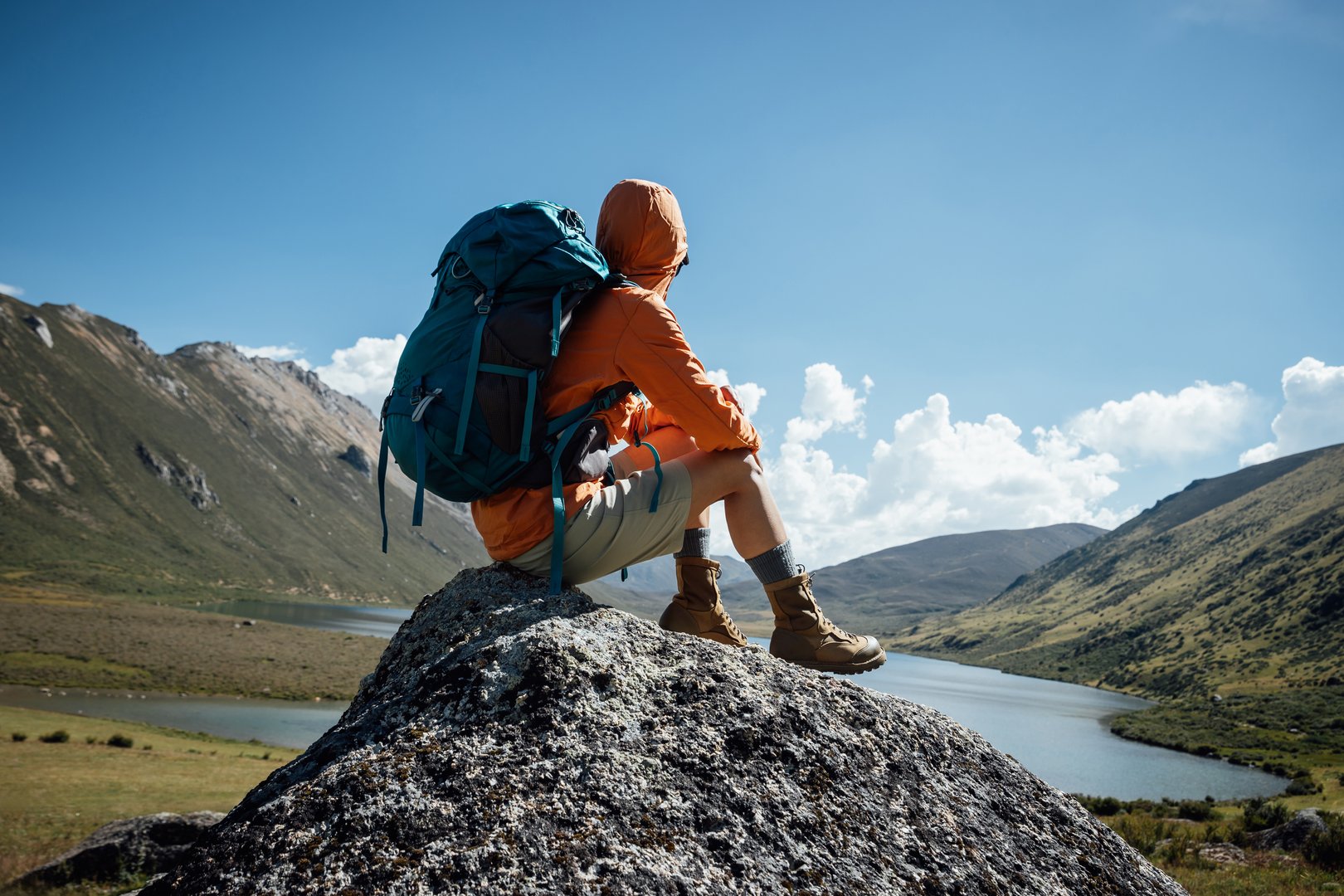 Backpacking woman sit on high altitude mountain top,enjoy the view of a lake in the distance