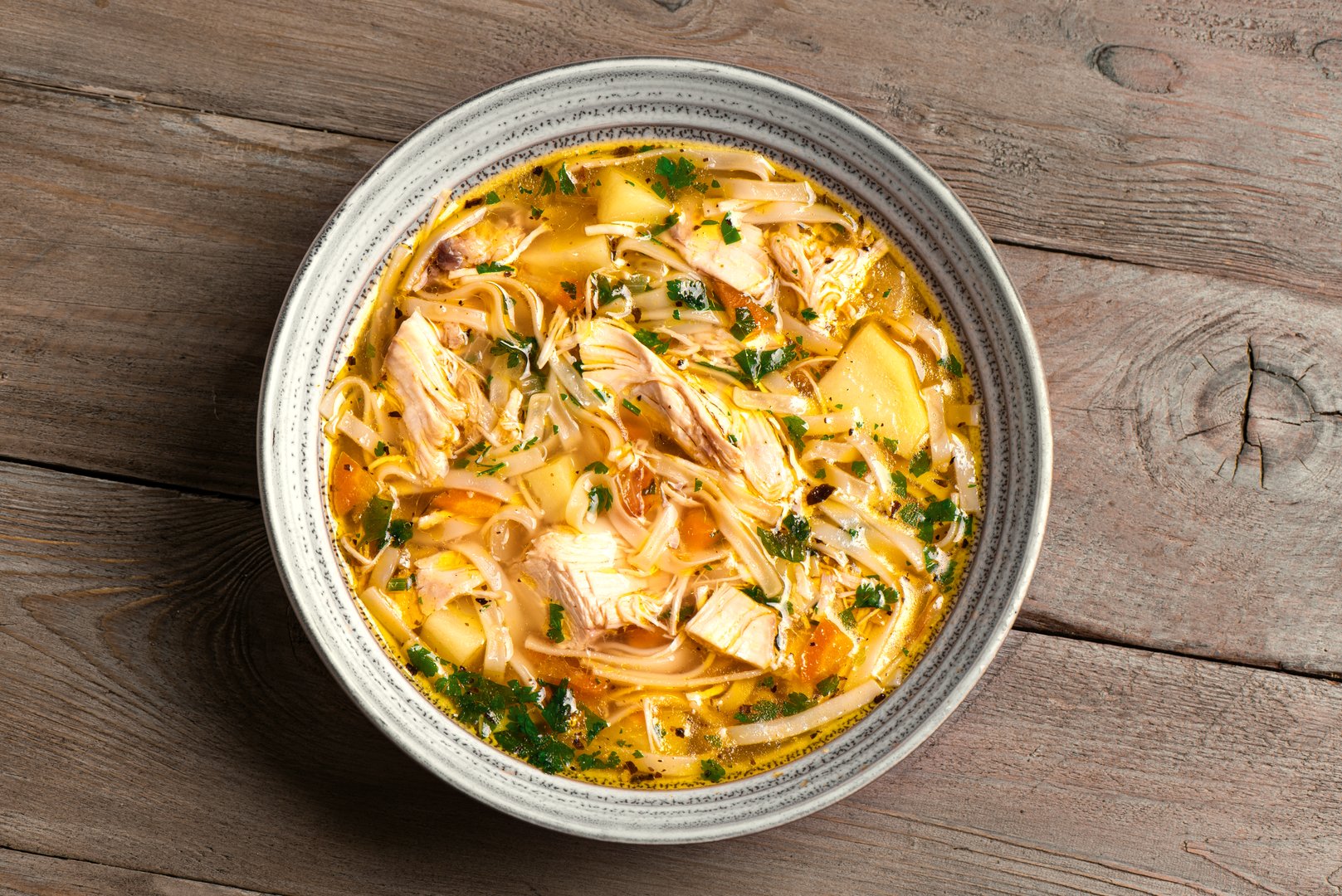 Homemade Chicken Noodle Soup on wooden background, top view. Bowl of hot chicken soup, healthy comfort food.