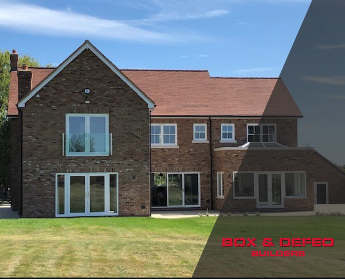 Modern luxury home exterior with large windows, stone facade, and spacious driveway at sunset.