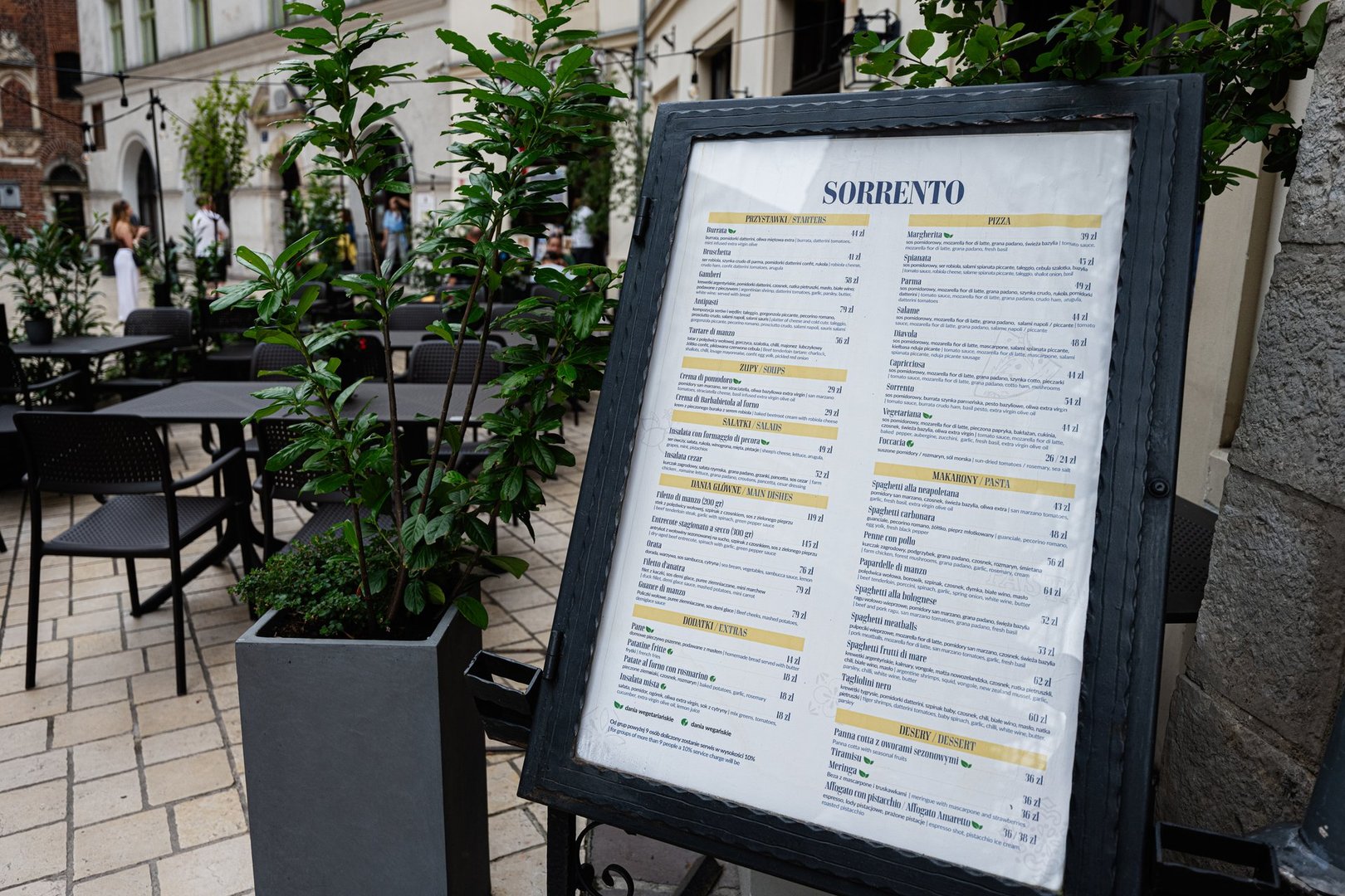 Krakow, Poland - July 08, 2025: Cafe Sorrento menu displayed on a stand in Krakow, Poland with seating arrangements nearby.