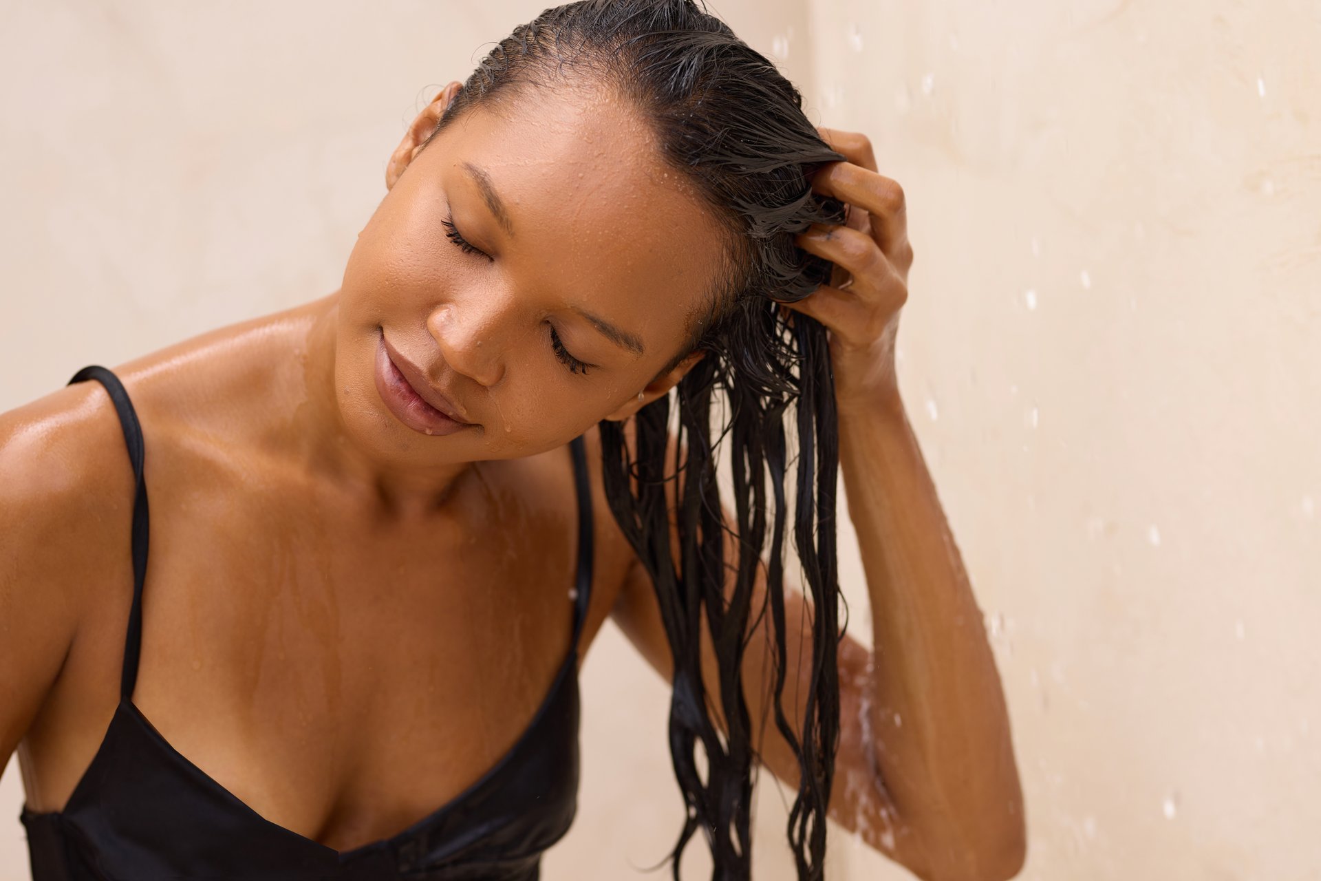 A woman is enjoying a refreshing hair wash in the shower, illustrating relaxation and self-care. The soothing water and her peaceful expression convey a relaxing personal grooming moment.