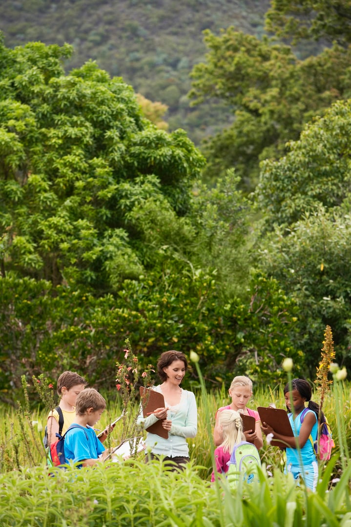 Young teacher with children preparing notes on clipboards during field trip