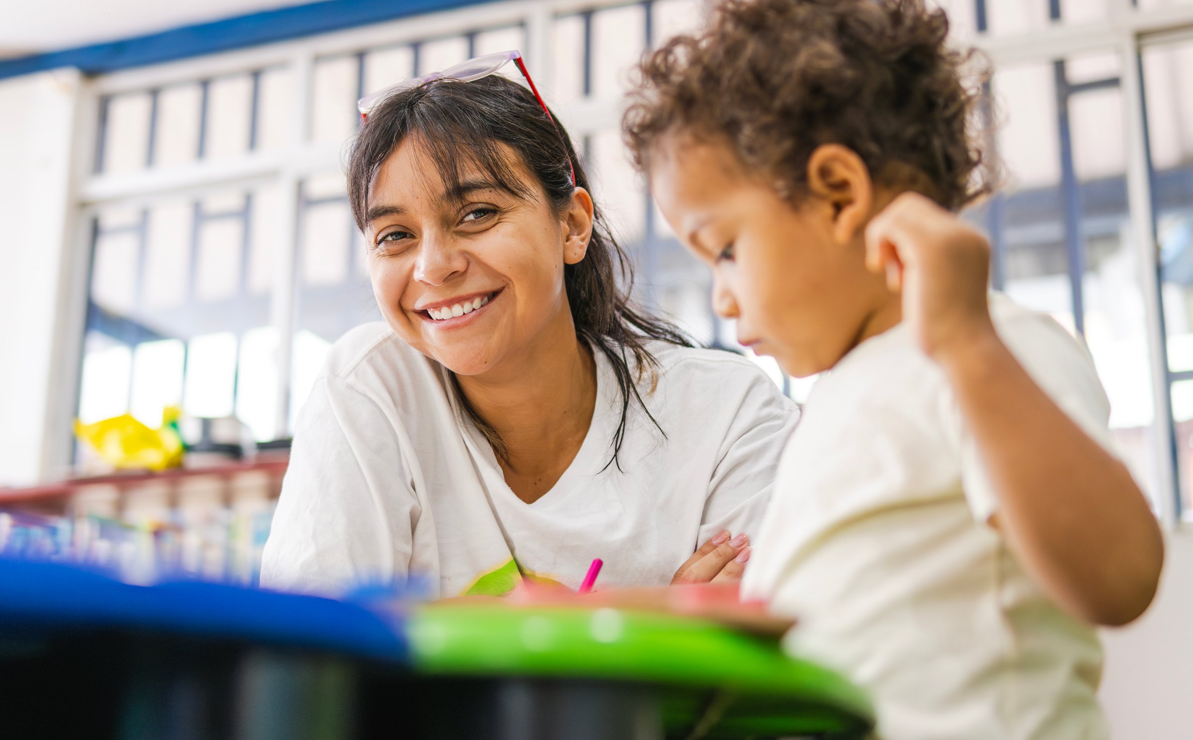 Happy latin american teacher smiling with child in preschool