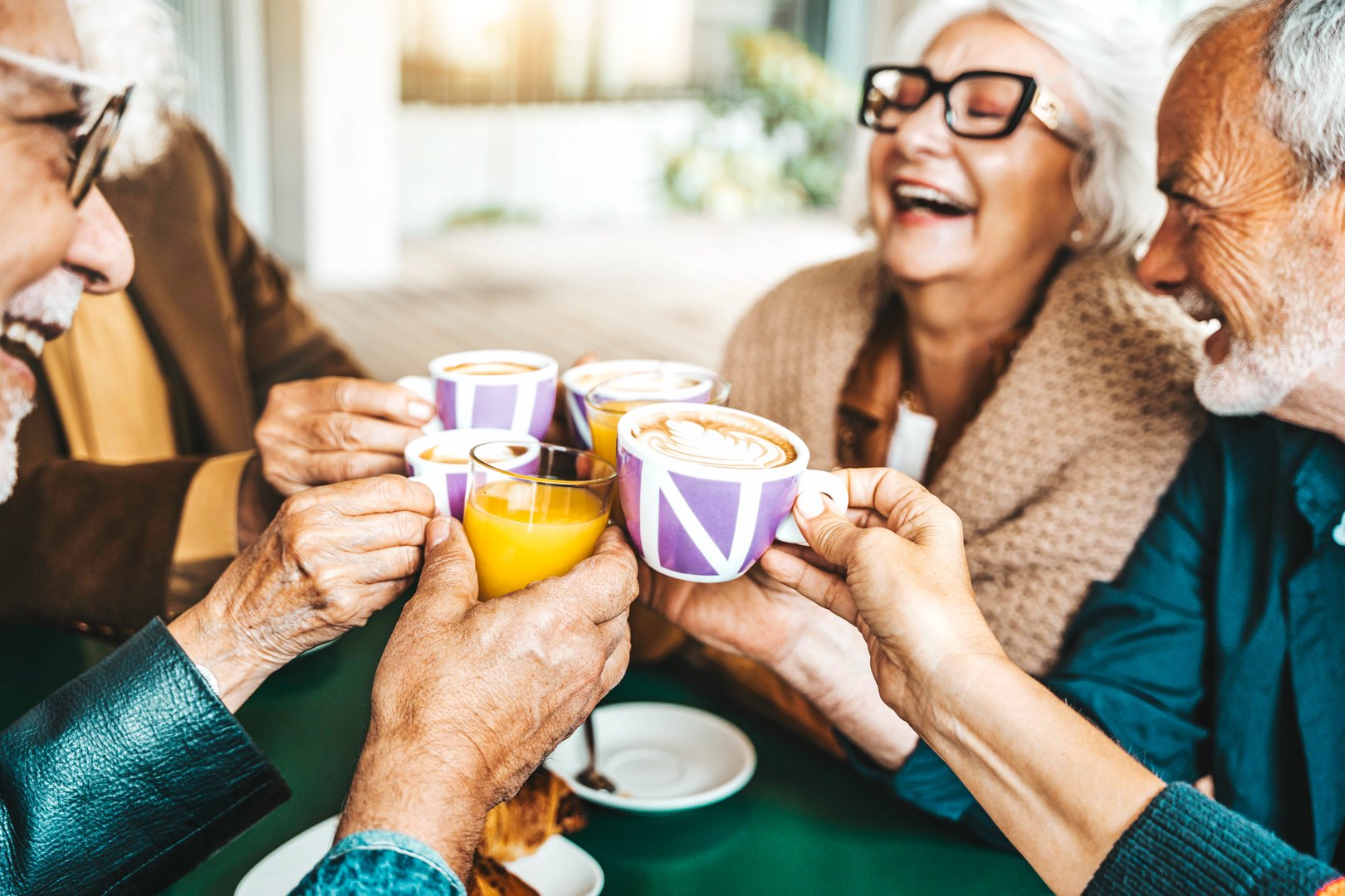 Senior people group toasting latte at coffee bar rooftop - Happy aged friends having fun together sitting at cappuccino restaurant - Life style concept with smiling men and women at cafe terrace