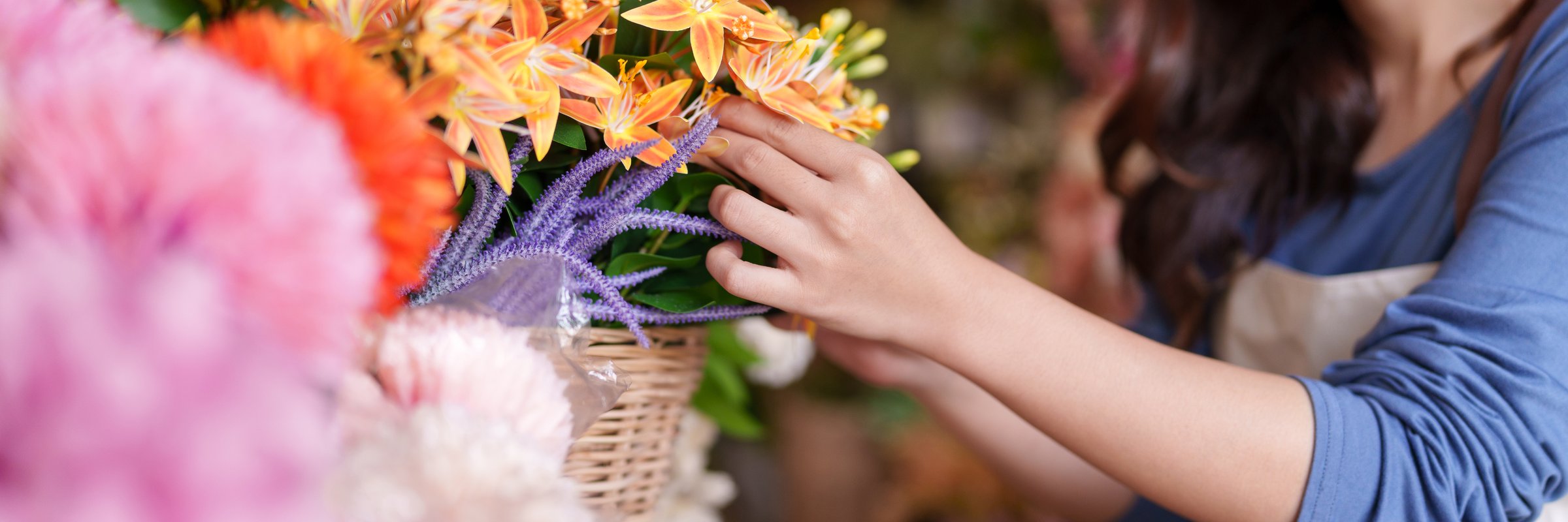 Skilled Asian florist carefully arranges vibrant artificial flowers in a charming basket perfect for home decor display