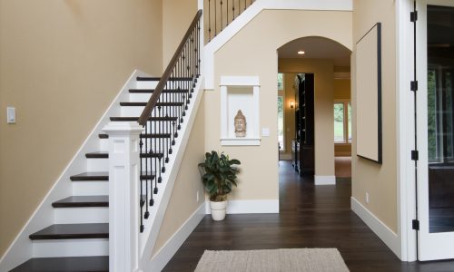 Modern home entryway with a staircase, beige walls, dark wood flooring, and a decorative niche with a small statue.