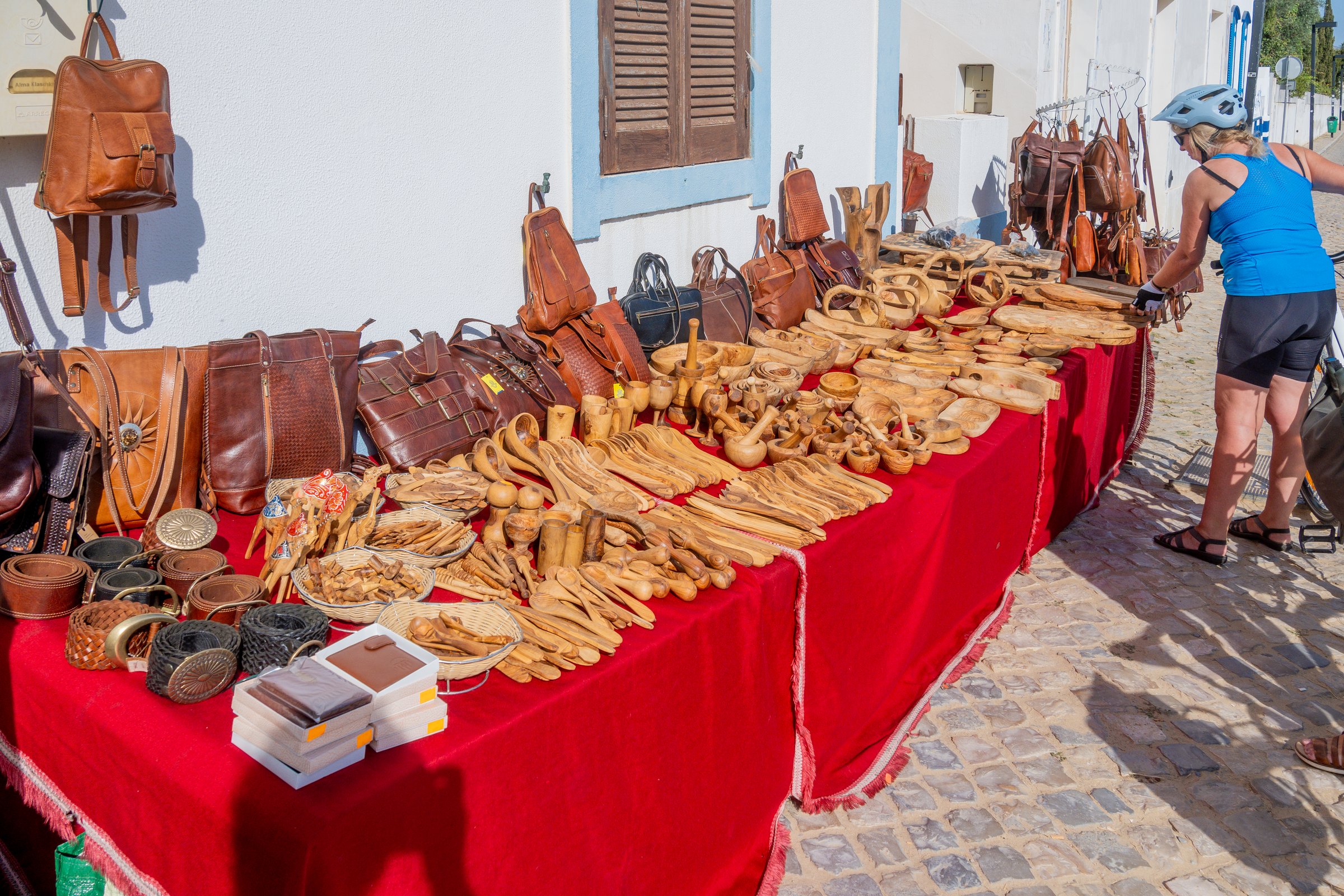 Cacela Velha, Algarve - Portugal - 09-15-2024: Market stand displaying handcrafted wooden items and leather goods on red cloth, including spoons, bowls, pipes, belts, and bags.