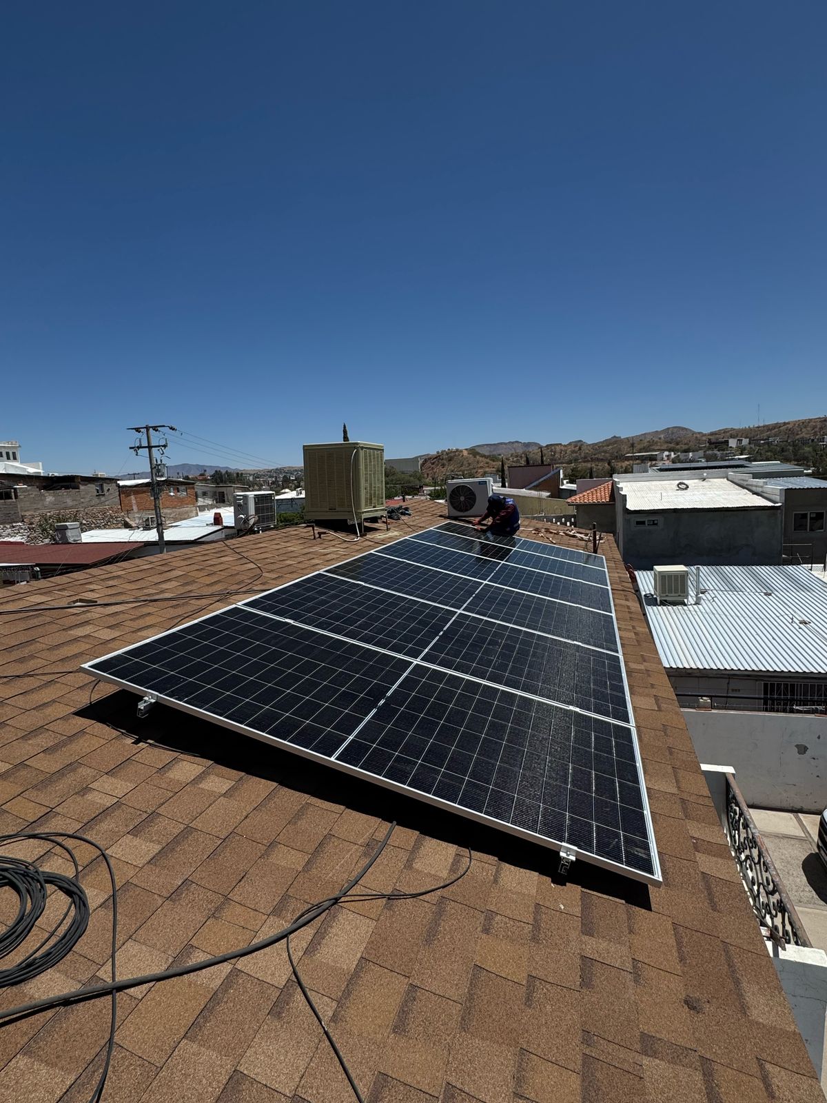 Worker installing solar panels on a rooftop under clear blue sky.