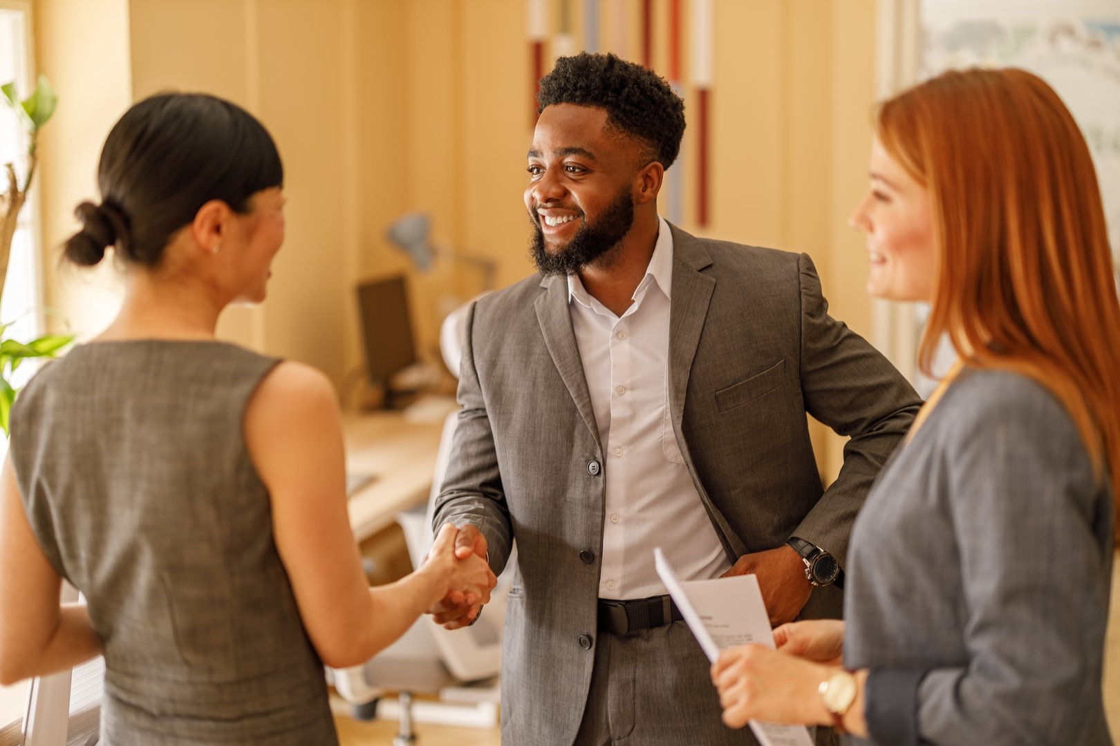 Male entrepreneur smiling and giving handshake to female partners sealing business deal in modern workspace
