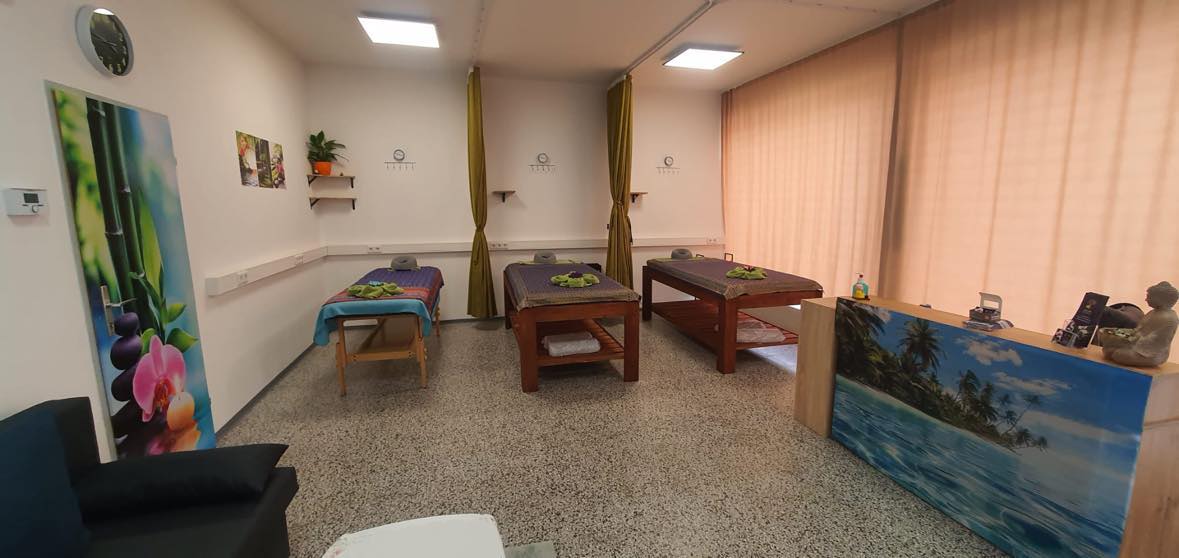 A serene massage room with three tables, curtains for privacy, nature-themed decor, and soft lighting.