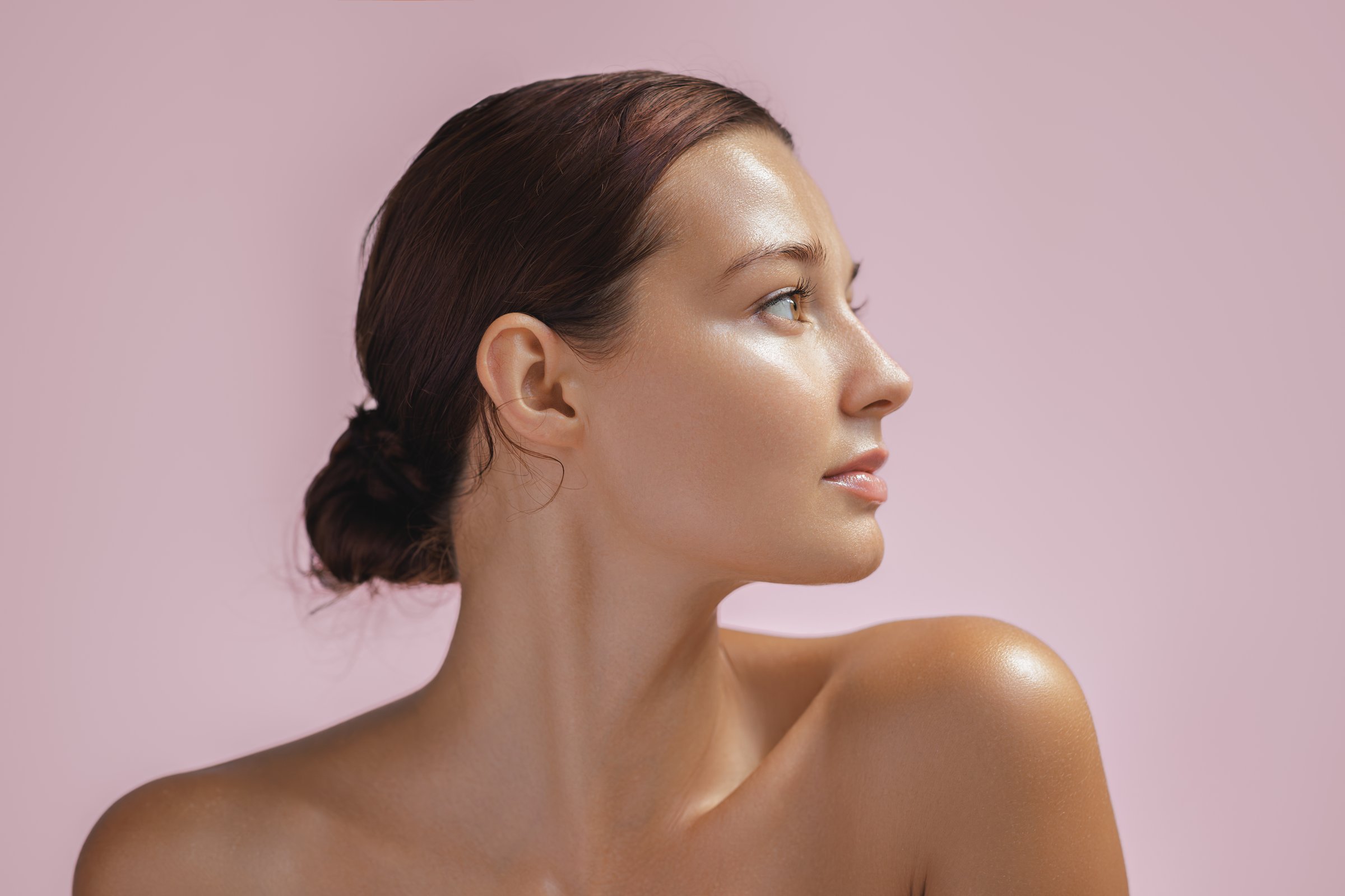 Beautiful young adult woman in profile with healthy shiny skin. Photo of gorgeous girl after morning beauty cosmetic routine finishes daily makeup on pink background. Youth and skin care concept