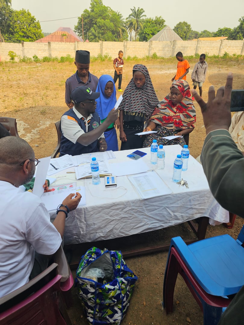 People registering for an event at an outdoor table with documents and water bottles, including children and adults.