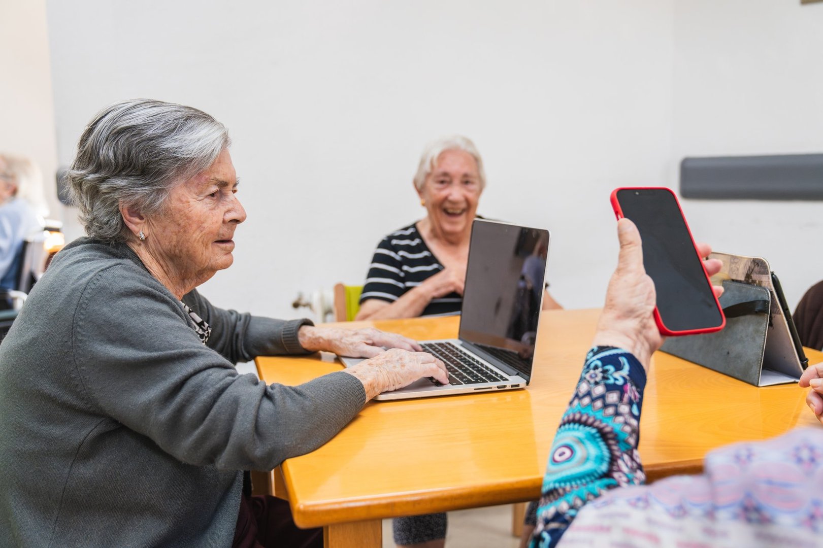 Senior women in a nursing home engaging with laptops and smartphones, enjoying moments of learning and connection
