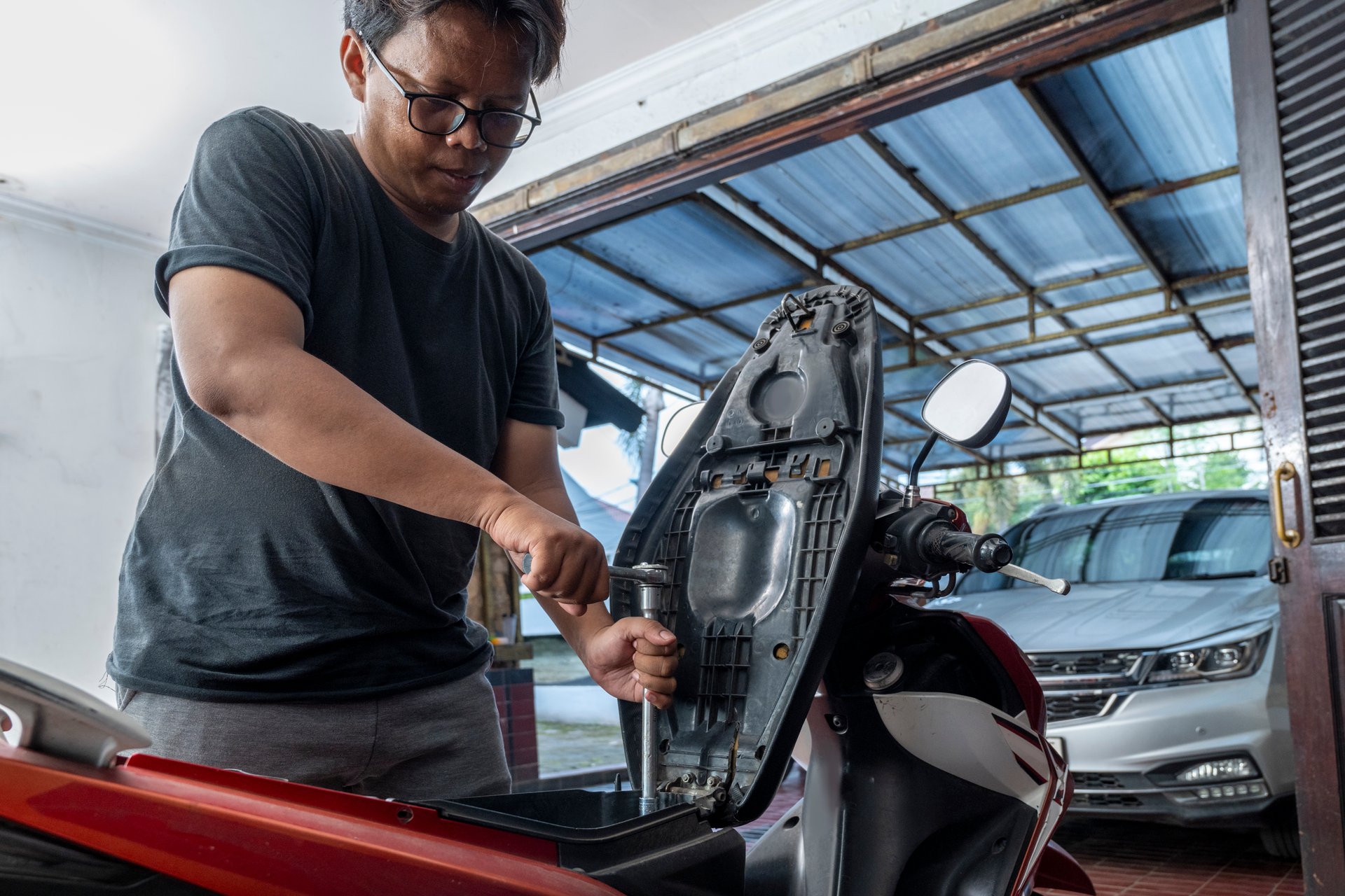Indonesian southeast asian repairman using a socket wrench tool to repair a motorcycle in a workshop