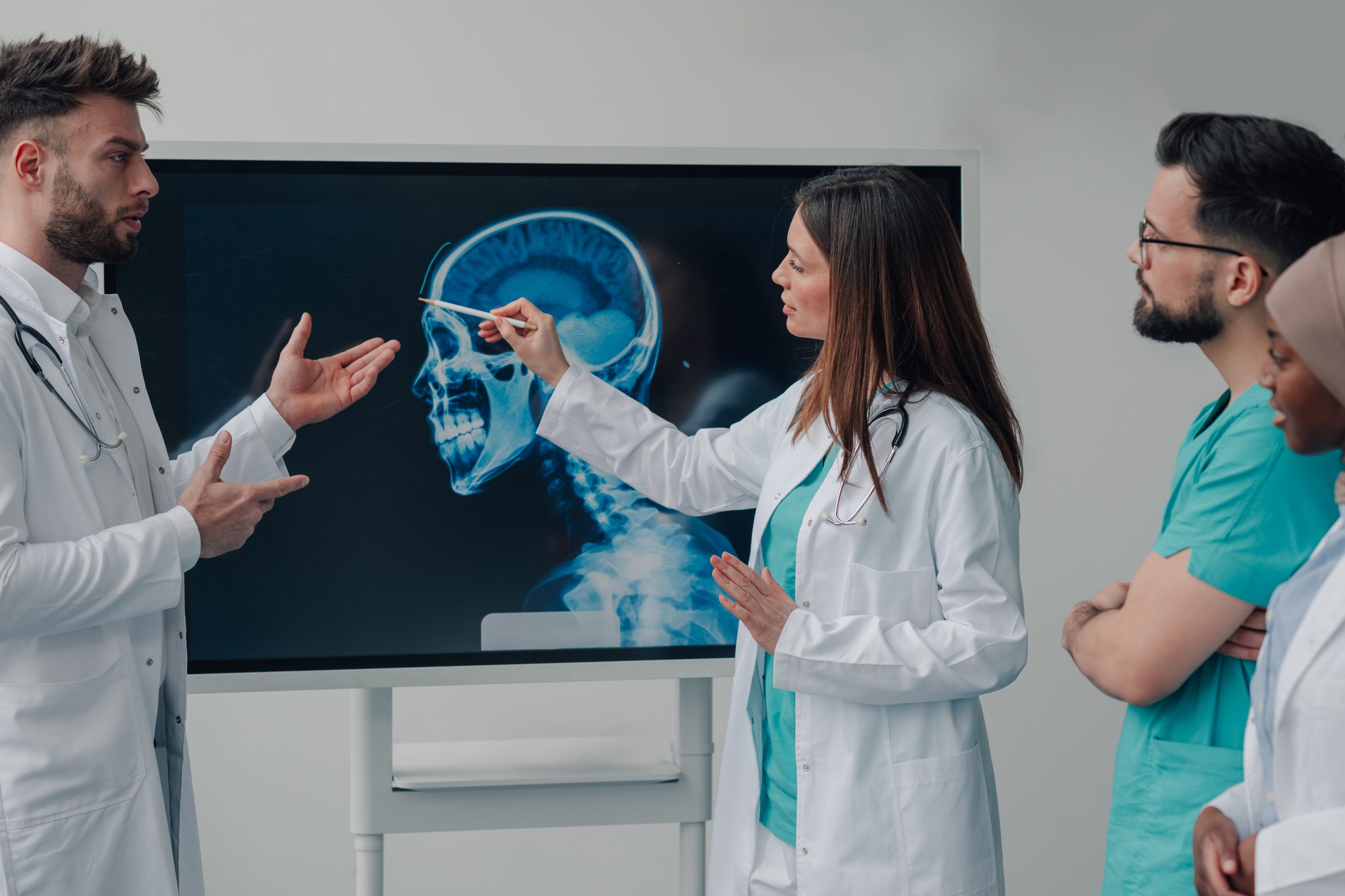 Doctors and nurses examining a head x-ray image on a monitor during a medical consultation