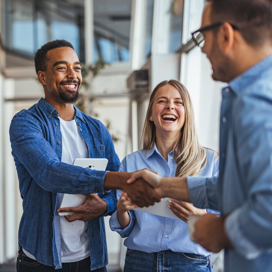 Happy coworkers in a modern office environment exchanging a handshake. The image portrays teamwork, success, and diversity in a professional setting, emphasizing positive relationships and collaboration.