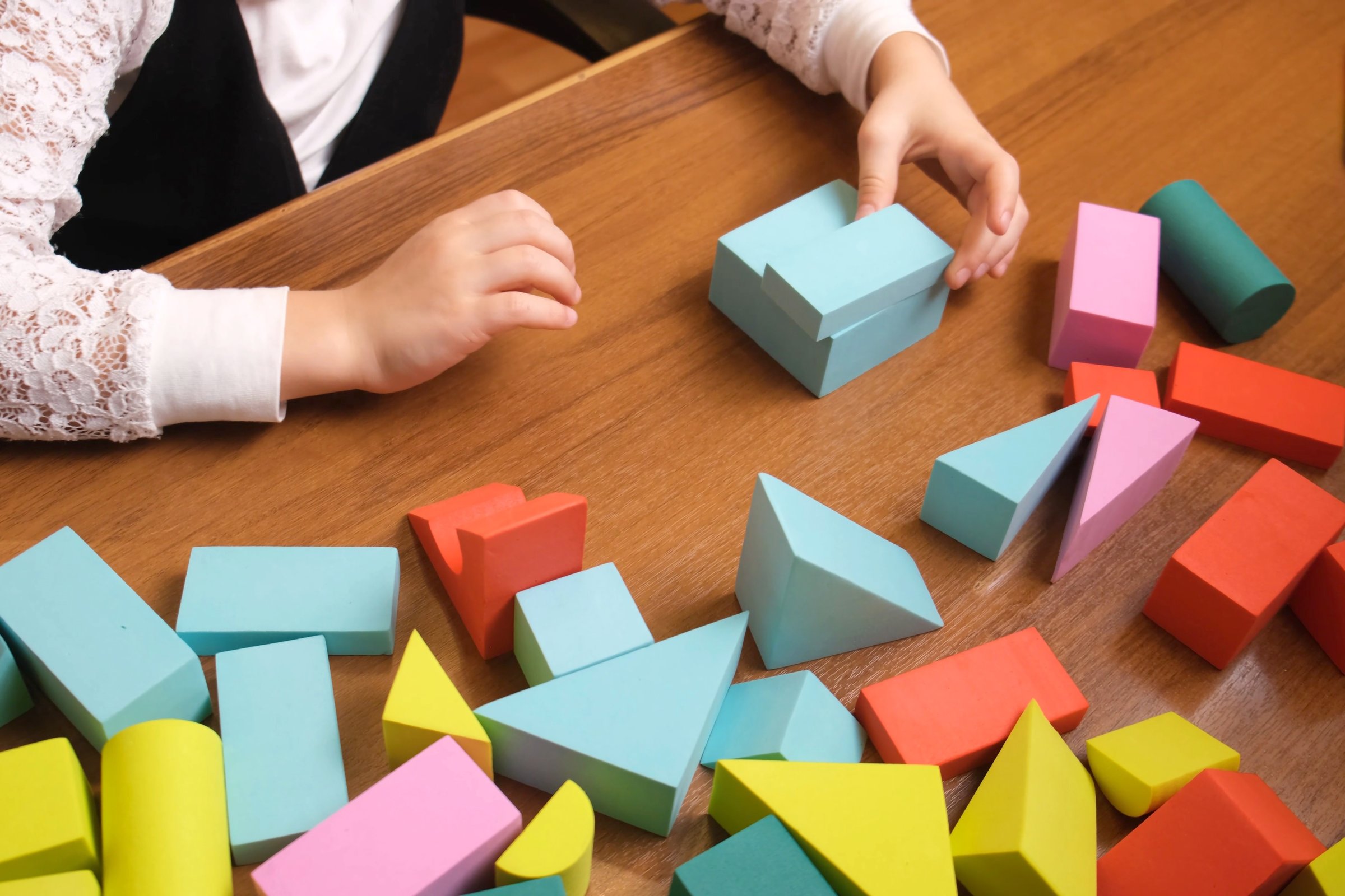 Little girls hands arranging colorful foam blocks on wooden table, building simple structure during quiet playtime, early learning scene for preschool materials, toy brands and parenting blogs