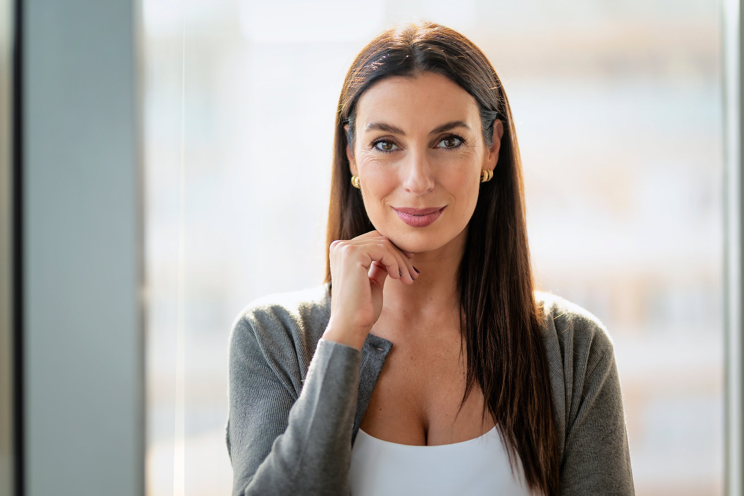 Attractive businesswoman standing in a modern office and smiling to the camera. Mid aged woman professional wearing business casual.