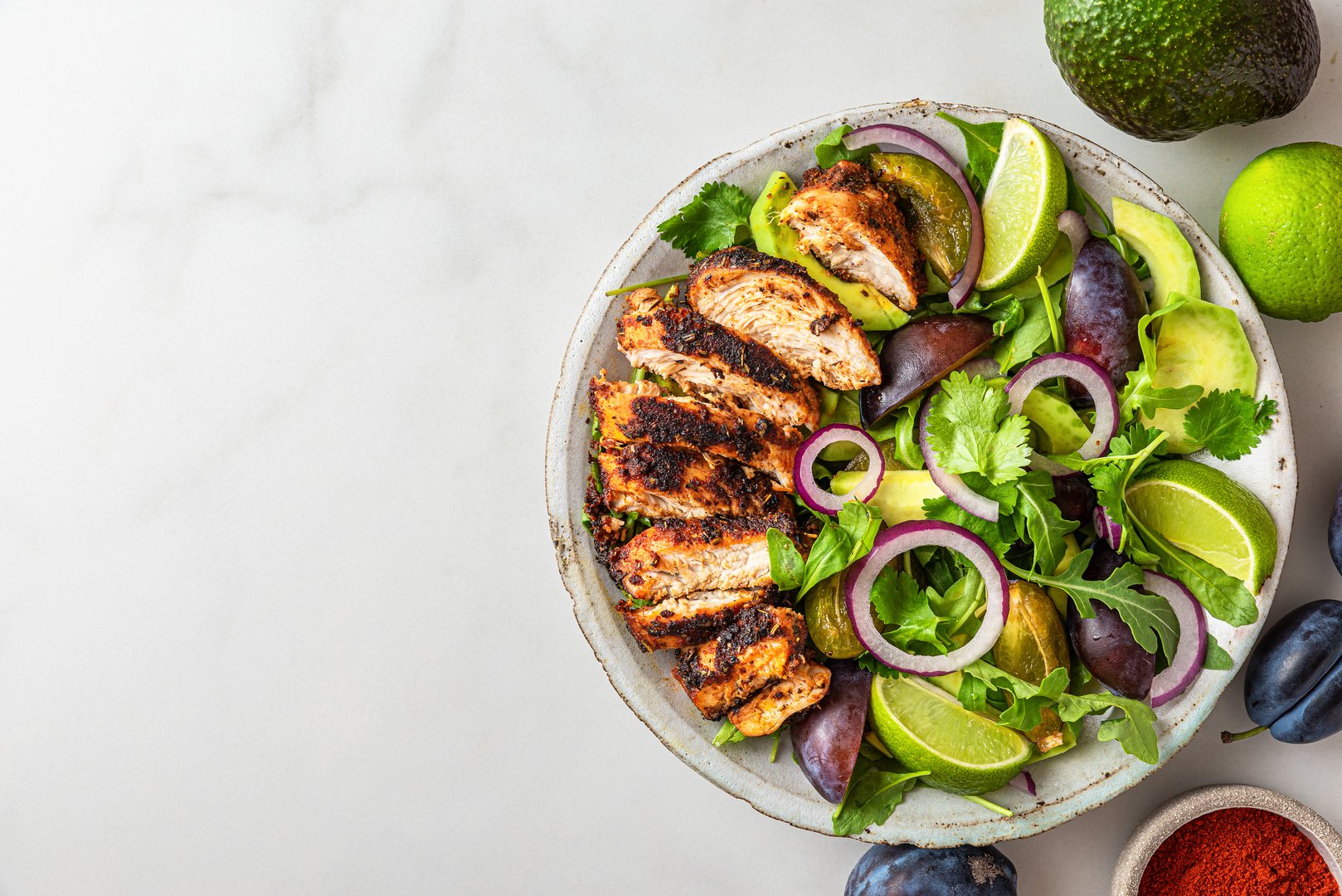 Grilled chicken fillet salad with arugula, avocado, plums, paprika, onion and lime in a plate on white background. Top view with copy space. Healthy diet food
