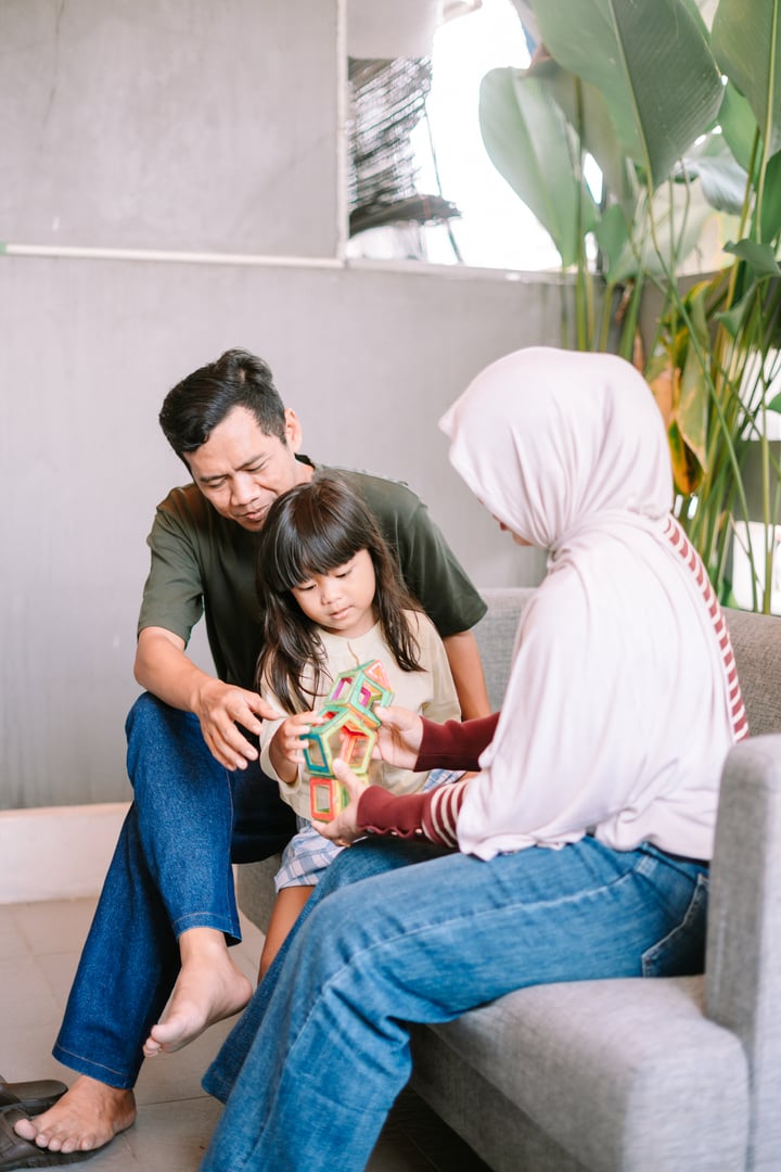 A loving family, including a father, mother in hijab, and their child, enjoys quality time building colorful magnetic blocks together in a cozy indoor setting, fostering creativity and bonding.